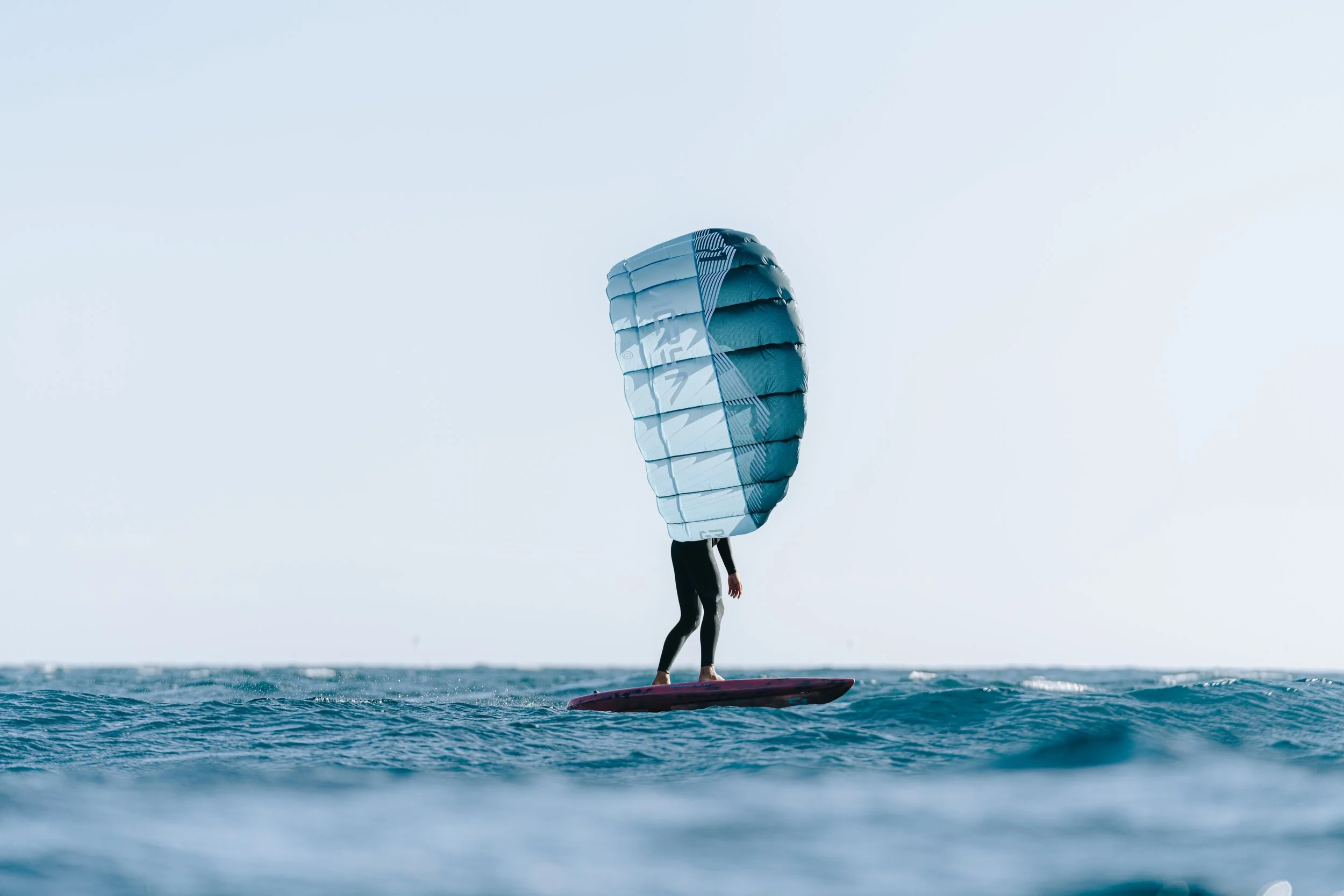Rider using Aeryn parawing on foil board riding small waves in the ocean
