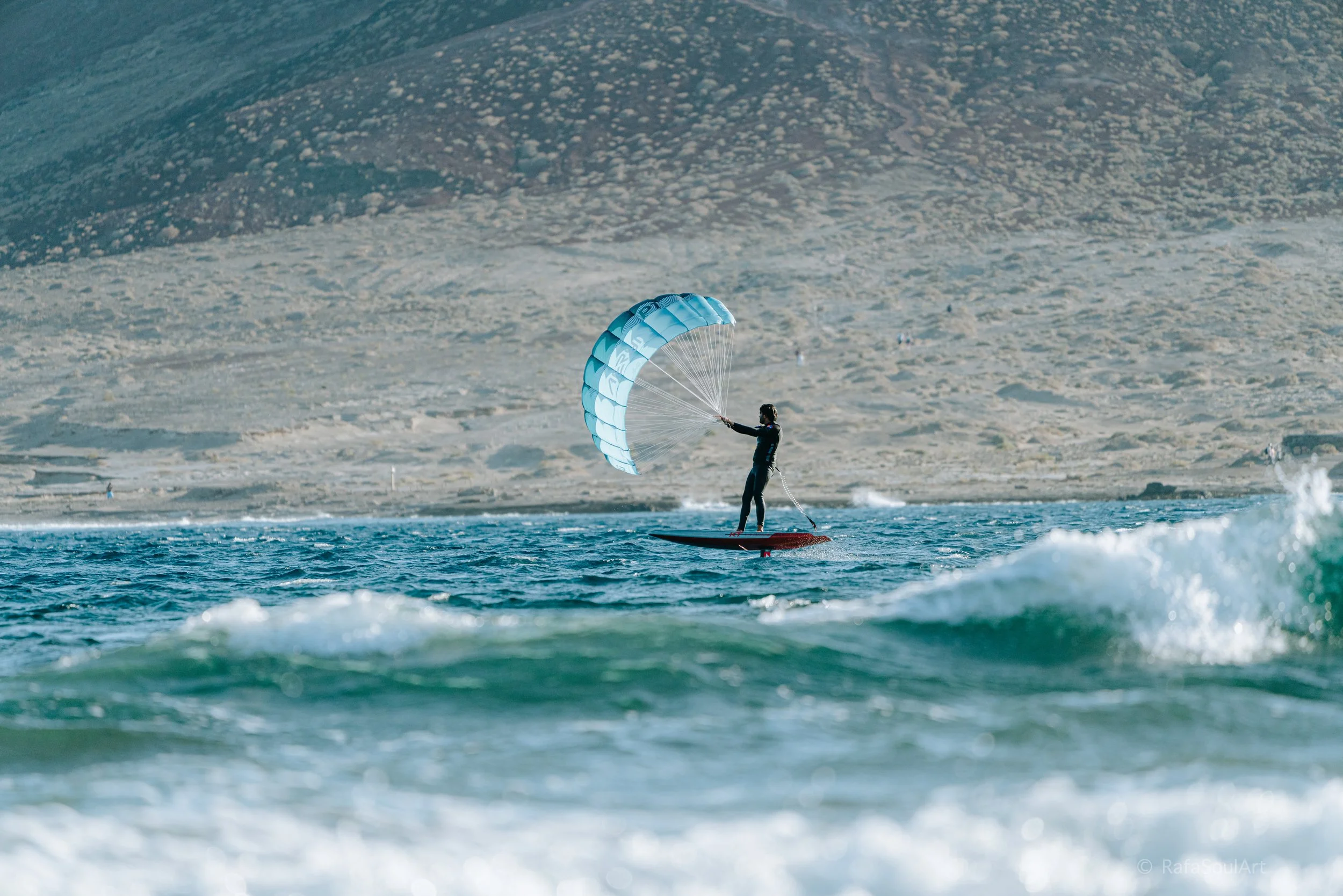 Rider using Aeryn parawing on foil board riding small waves in the ocean