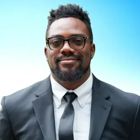 Man in suit with glasses and black tie smiling