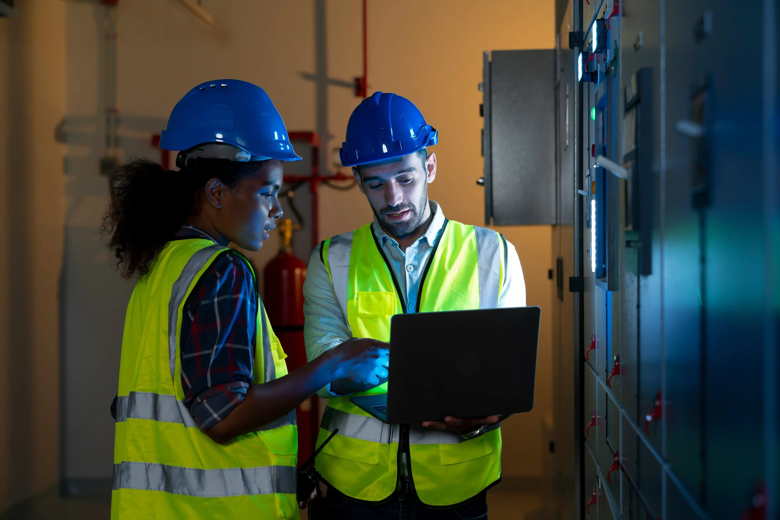 Energy auditors in safety gear using a laptop to assess efficiency in an industrial facility