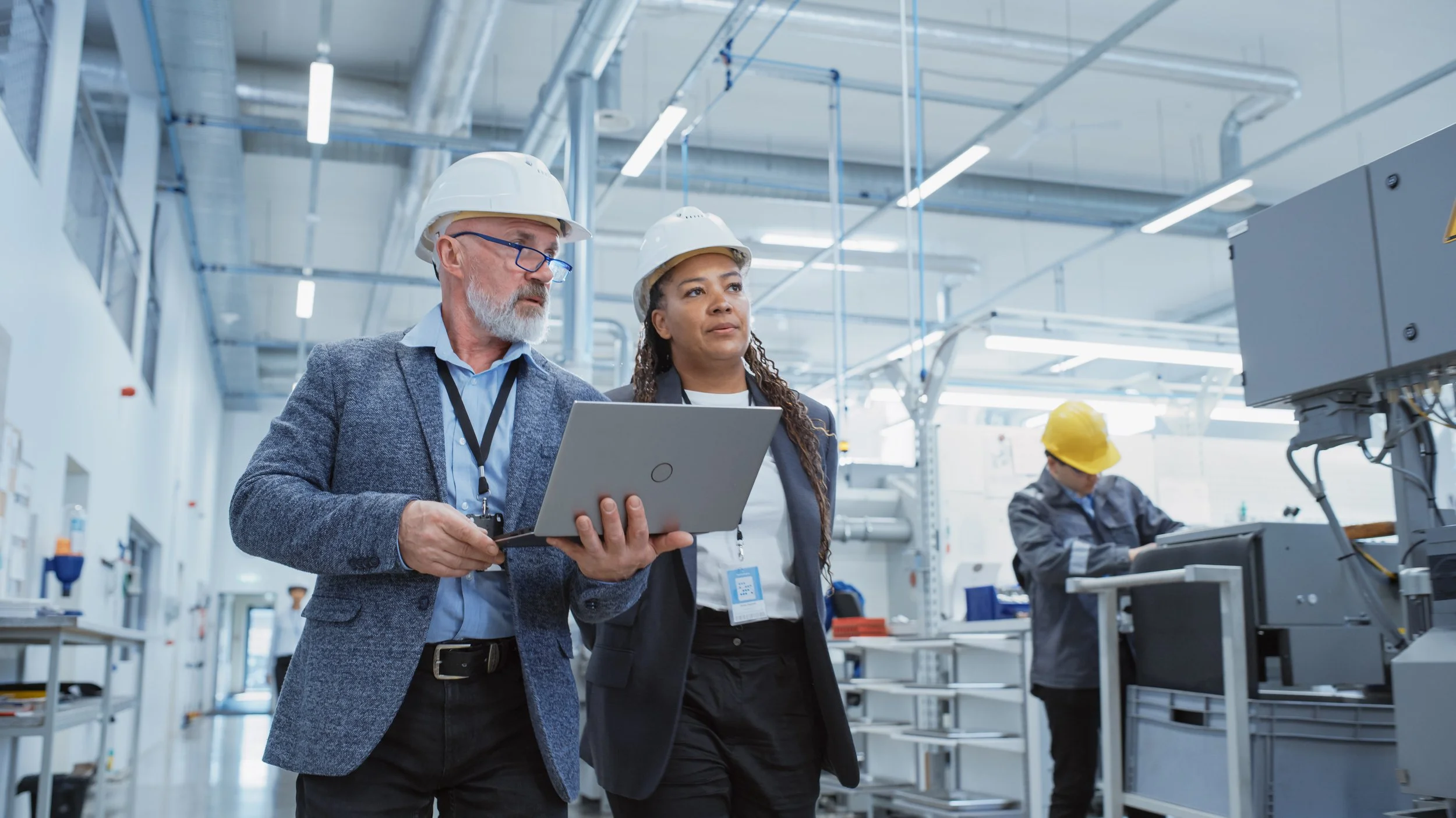 Energy auditors inspecting equipment with a laptop in a modern industrial or manufacturing facility.