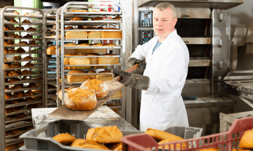 Baker placing a freshly baked loaf on a cooling rack in a bakery kitchen, showcasing energy-efficient kitchen equipment and optimized bakery operations.