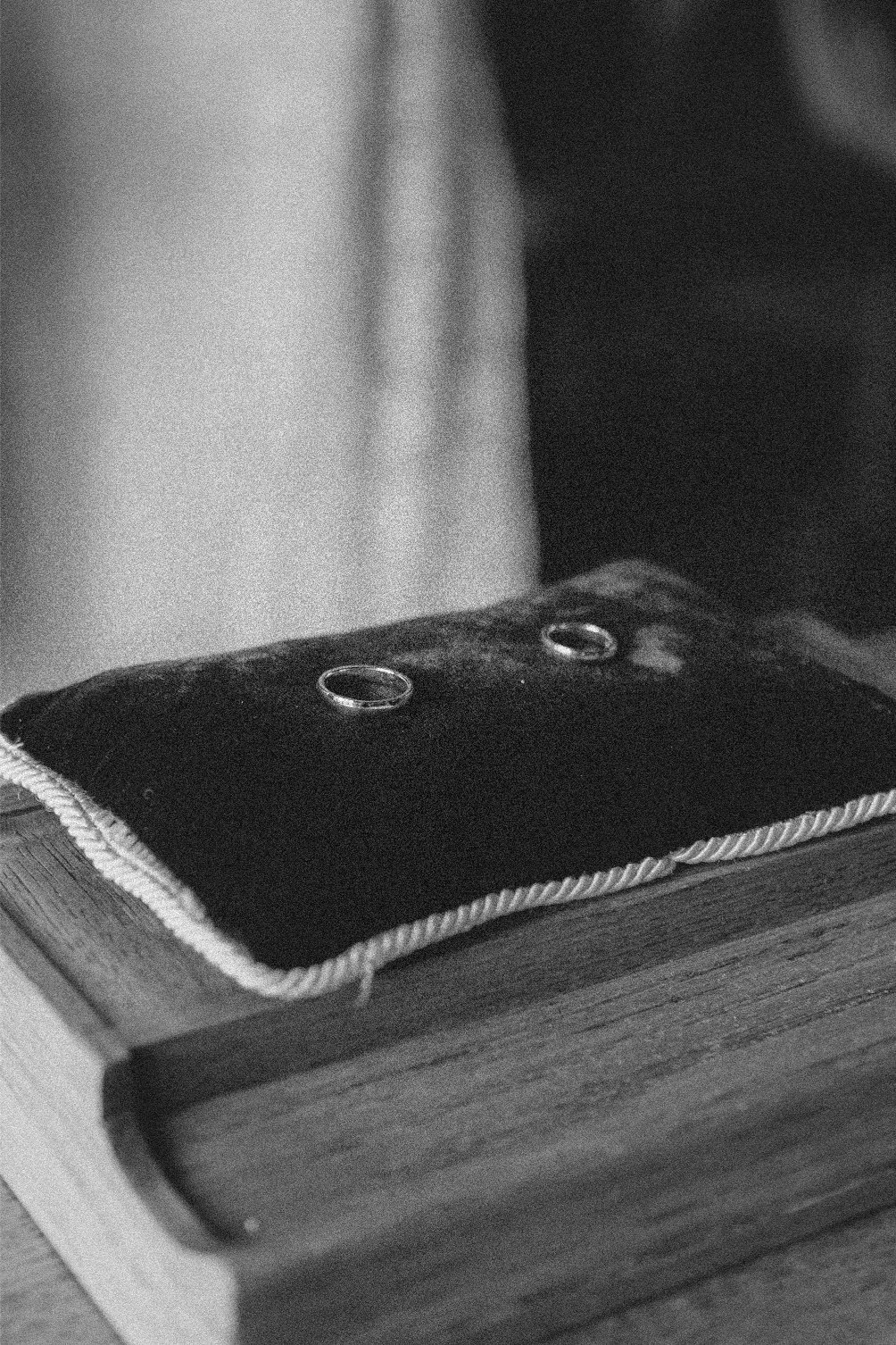 A black and white photo of a wooden table with a framed photo on top and a black cloth with metal grommets. The cloth has a textured edge.