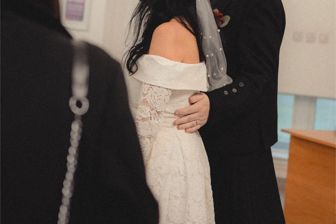 A bride and groom holding hands during their wedding ceremony, with an officiant visible in the foreground.