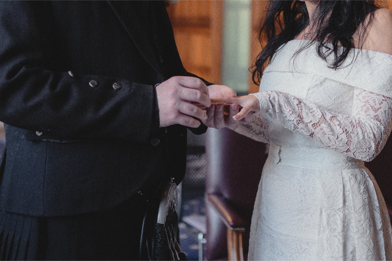 A couple exchanging wedding rings during a wedding ceremony, with the focus on their hands and wedding dress and suit.