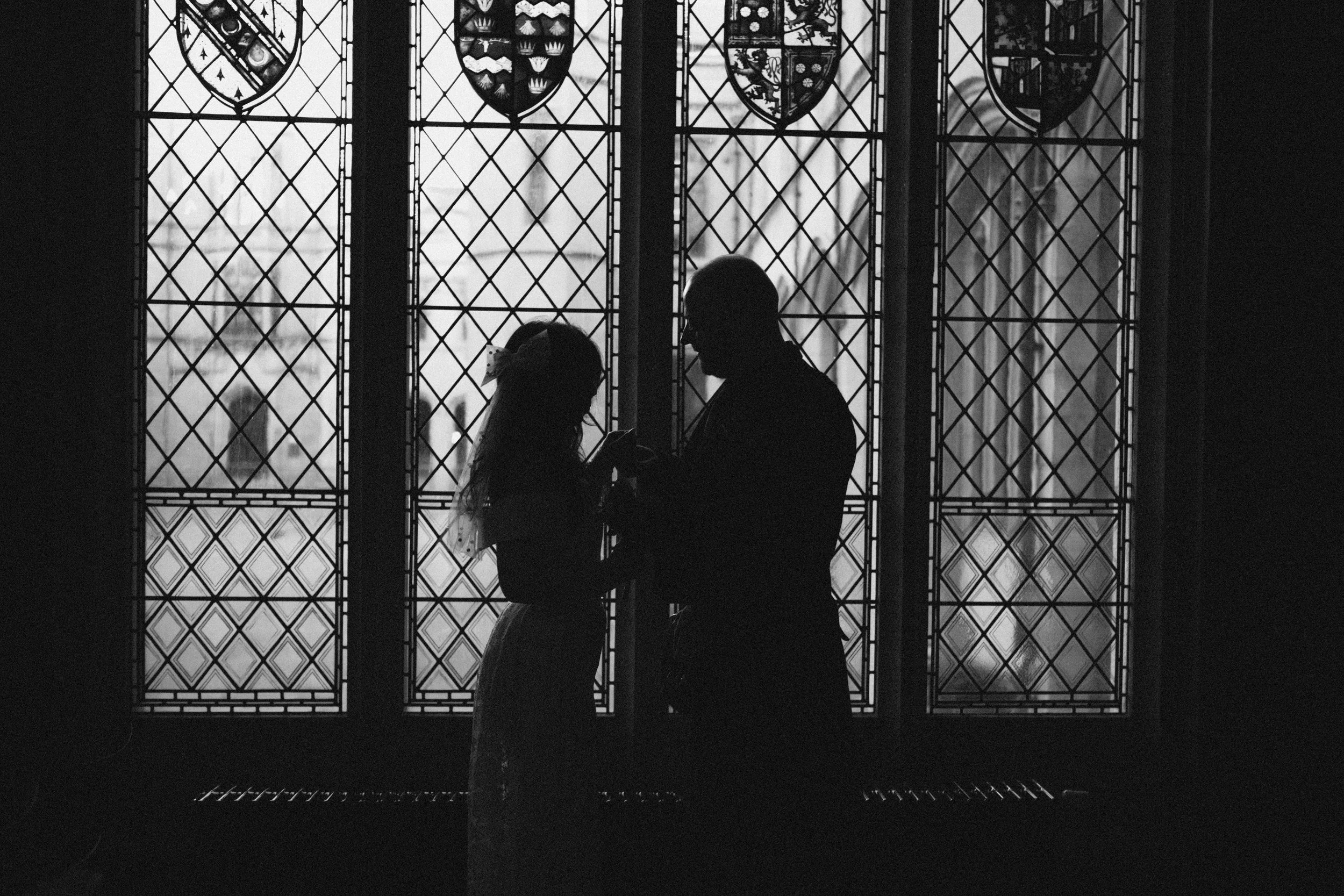 Silhouette of a man and a woman holding hands, standing in front of stained glass windows inside a church or cathedral.