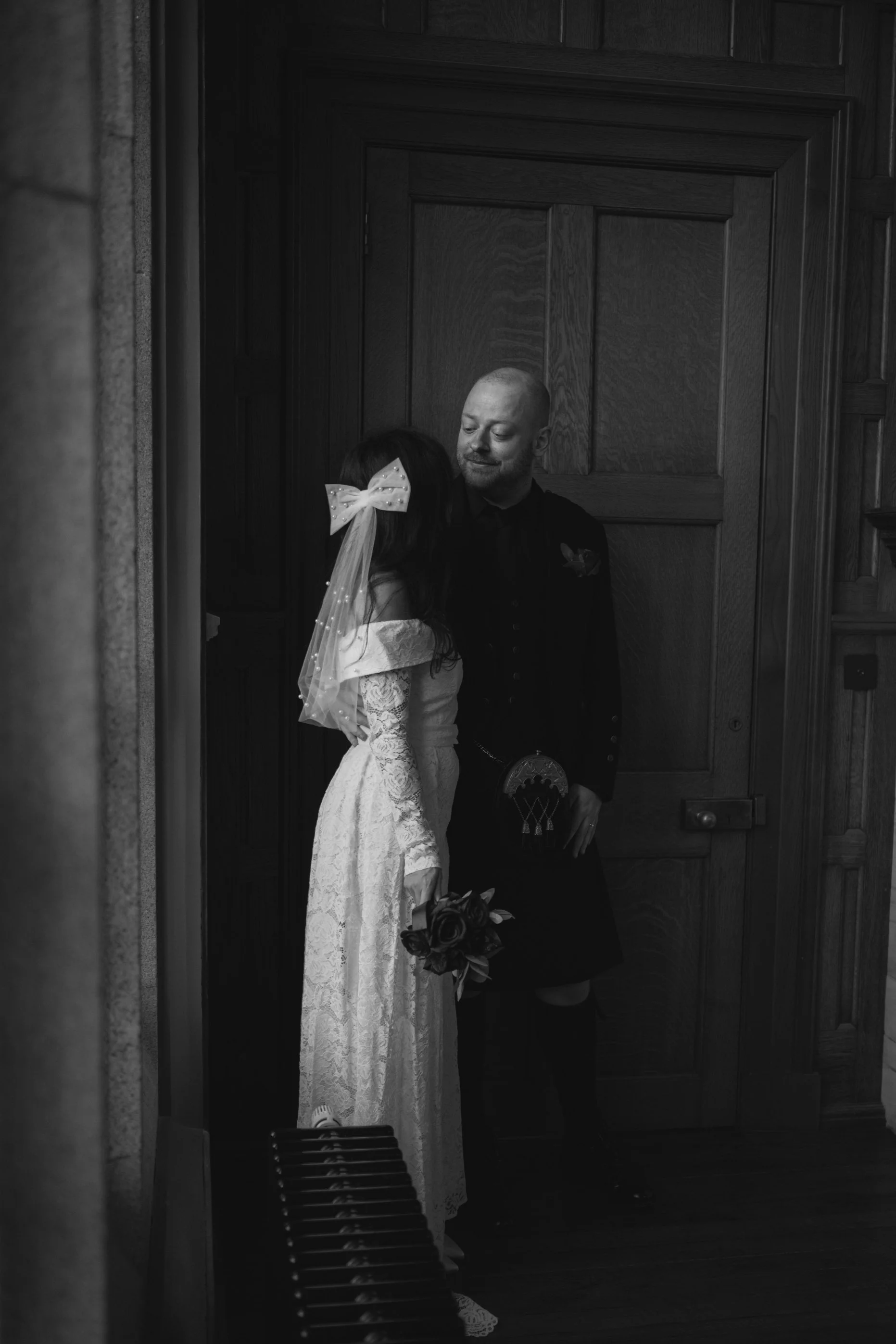 A bride and groom sharing a kiss in a wooden-paneled room during their wedding.