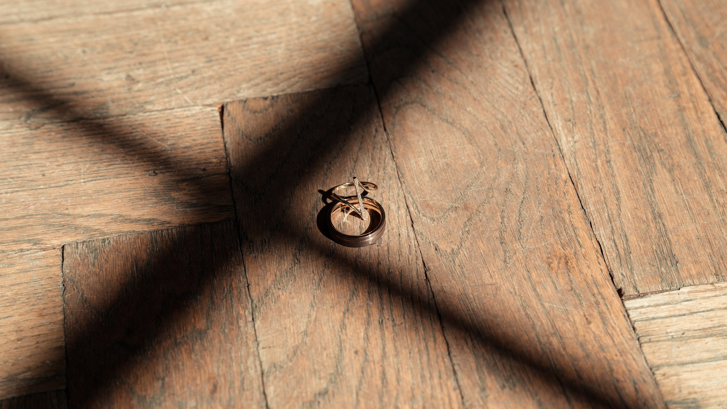 A pair of rings, one dark and one light, placed on a wooden surface, partially illuminated by sunlight creating shadows.