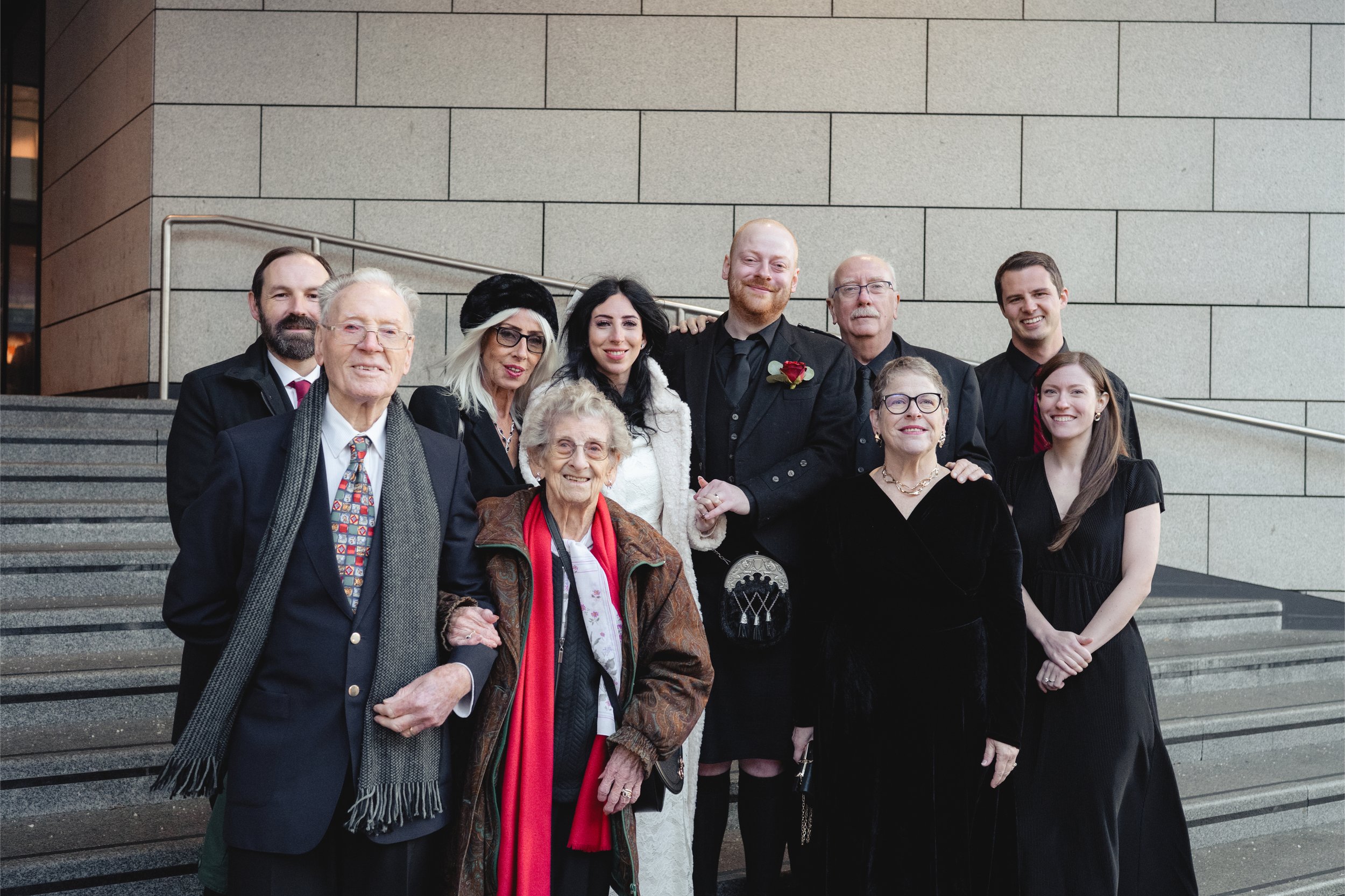A group of people dressed formally, gathered on steps outside a building for a celebration or event.