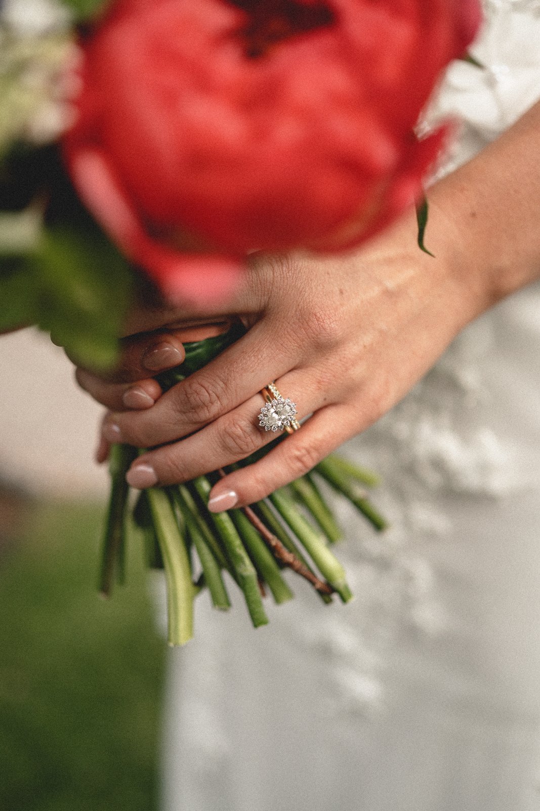 Close-up of a woman's hand holding a bouquet of red roses, showing an engagement ring with a large diamond on her finger.