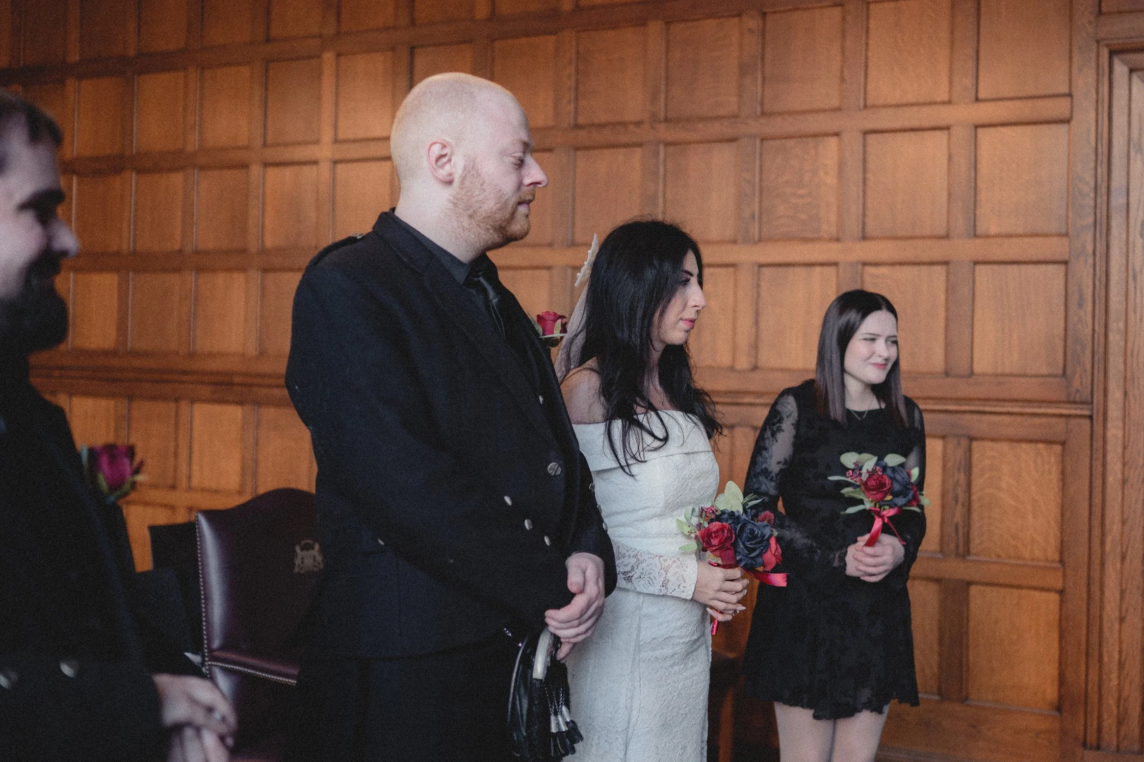 A group of people standing in a wood-paneled room, holding small bouquets of flowers, appearing to participate in a formal ceremony.