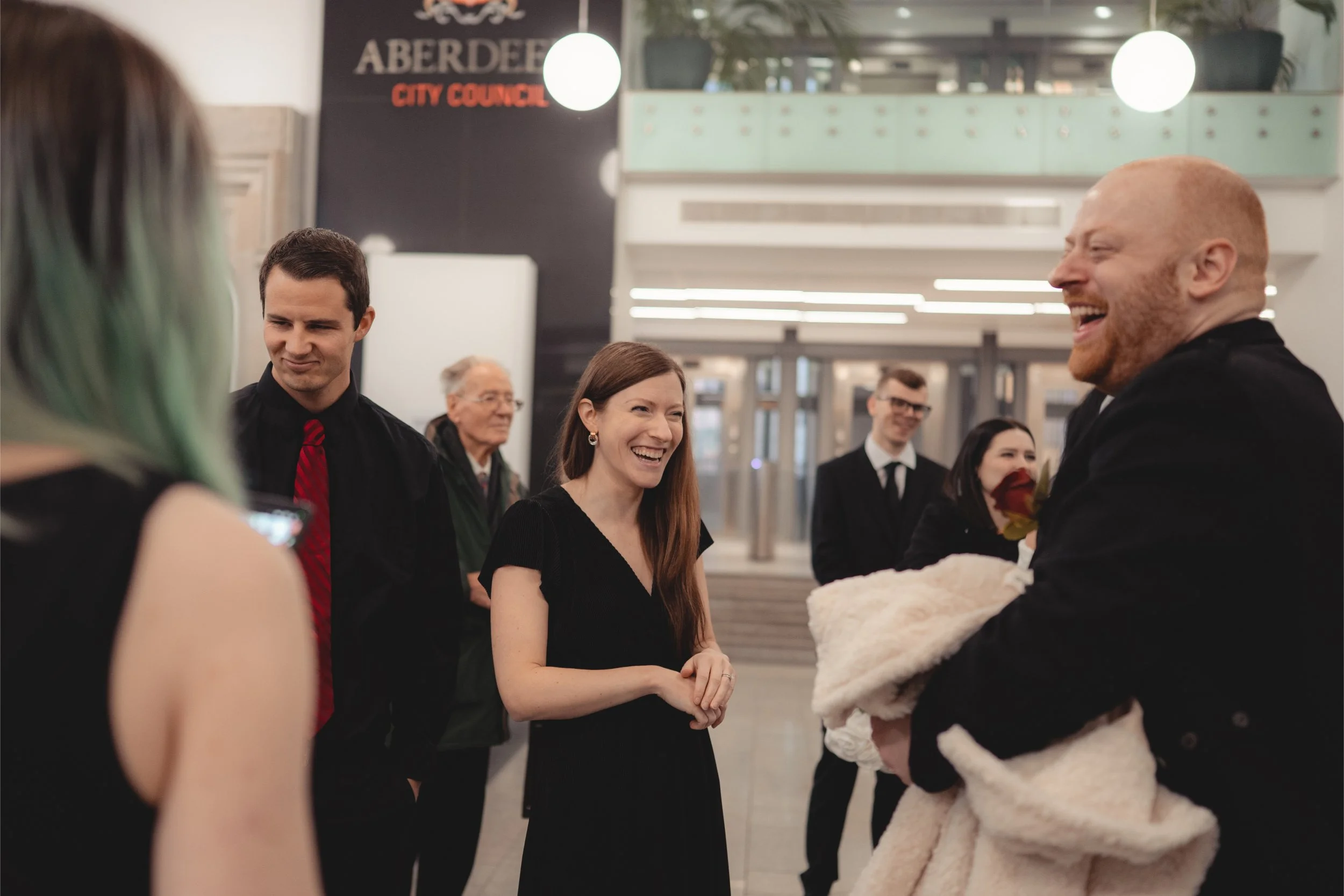 People smiling and talking in a lobby area with a sign that reads 'Aberdeen City Council' in the background.