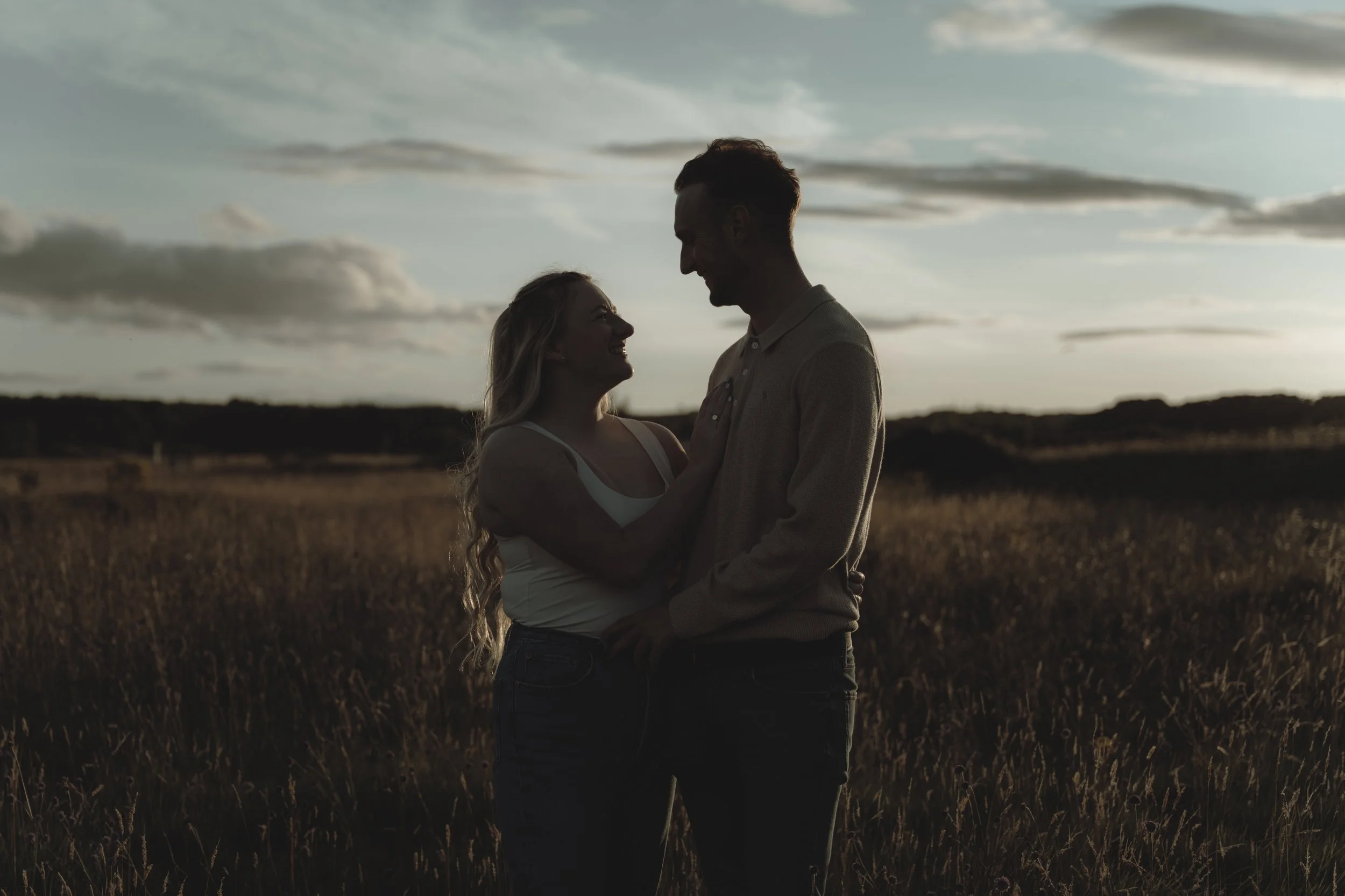 A couple holding each other and smiling at sunset in a field.