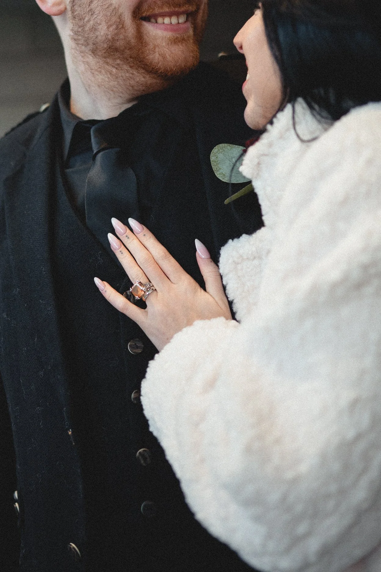 A woman with a ring on her finger is touching a man's chest, both smiling and close to each other, showing affection.