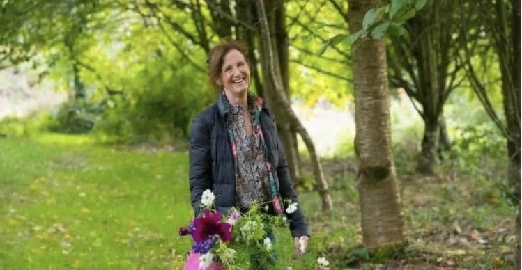 A woman holding a bouquet of flowers, standing outdoors in a forested area.