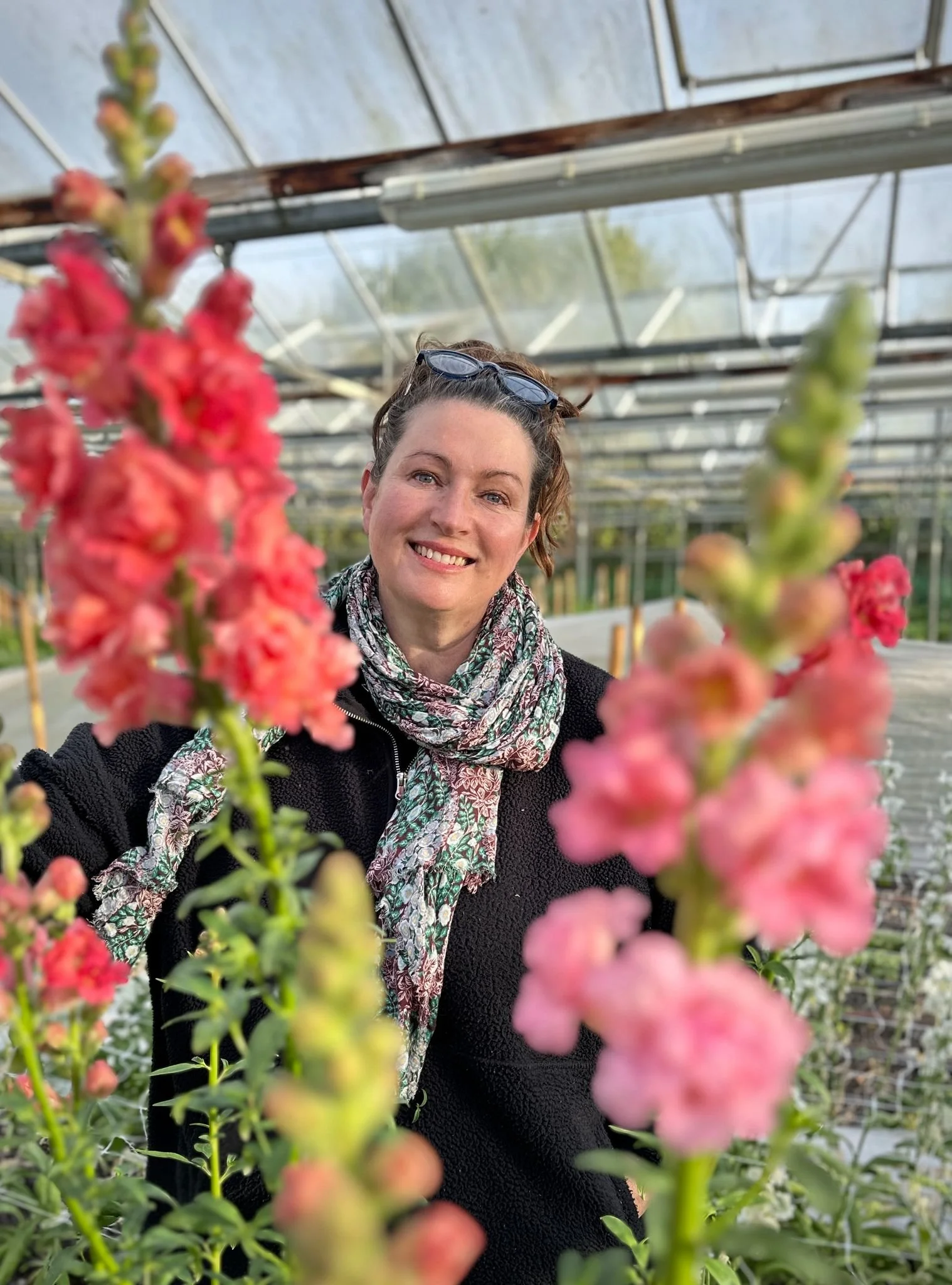 Woman in a greenhouse holding a large pink and peach dahlia flower.