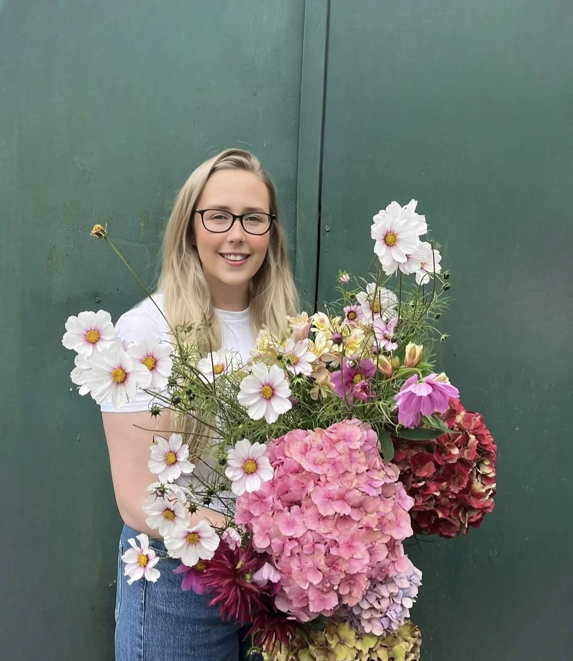 Irish flower farmer holding a large bouquet of colorful flowers against a green background.