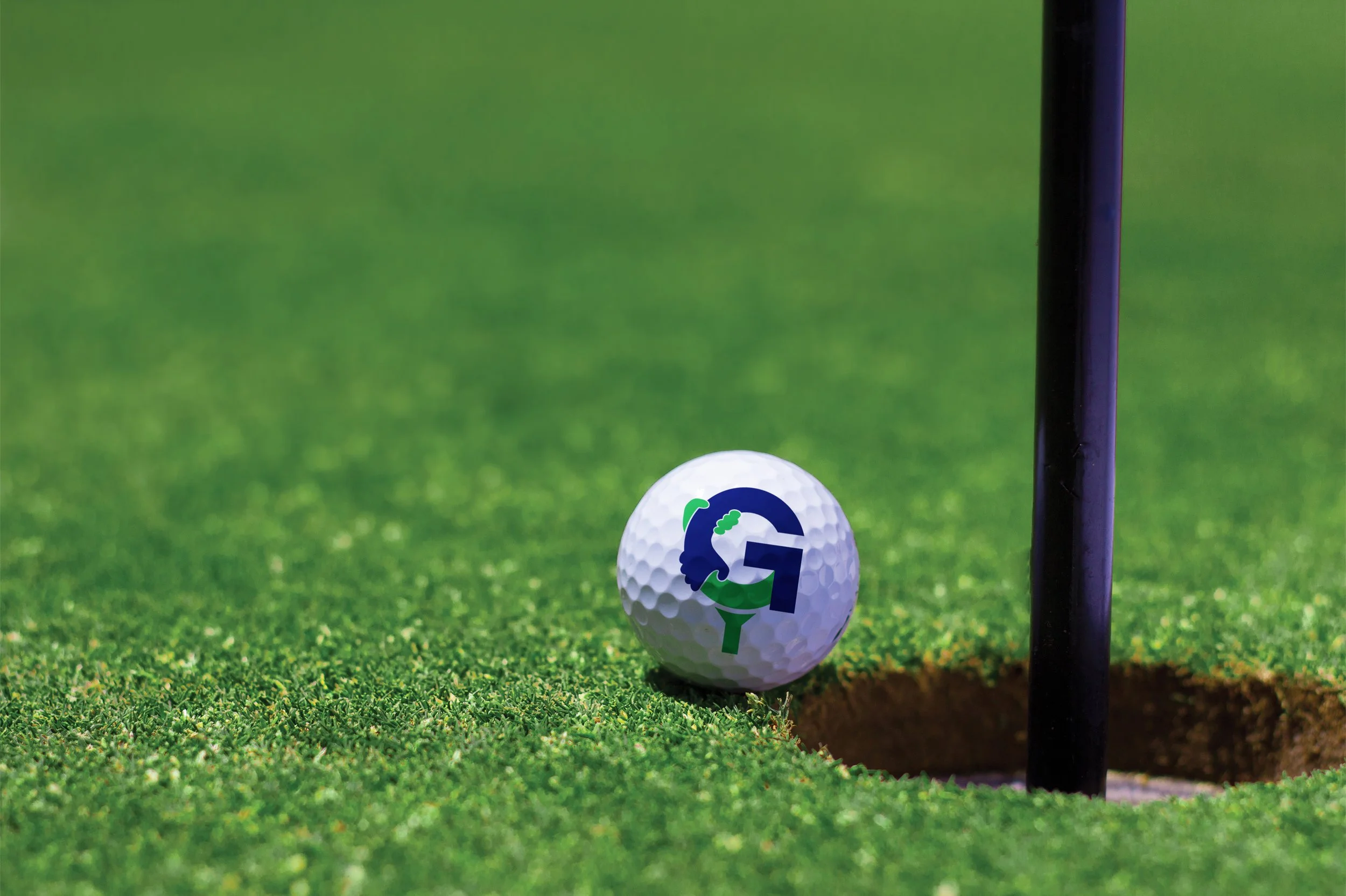 Close-up van een golfbal met een logo vlak naast de hole op een putting green. logo ontworpen door professioneel ontwerper branding and boosting