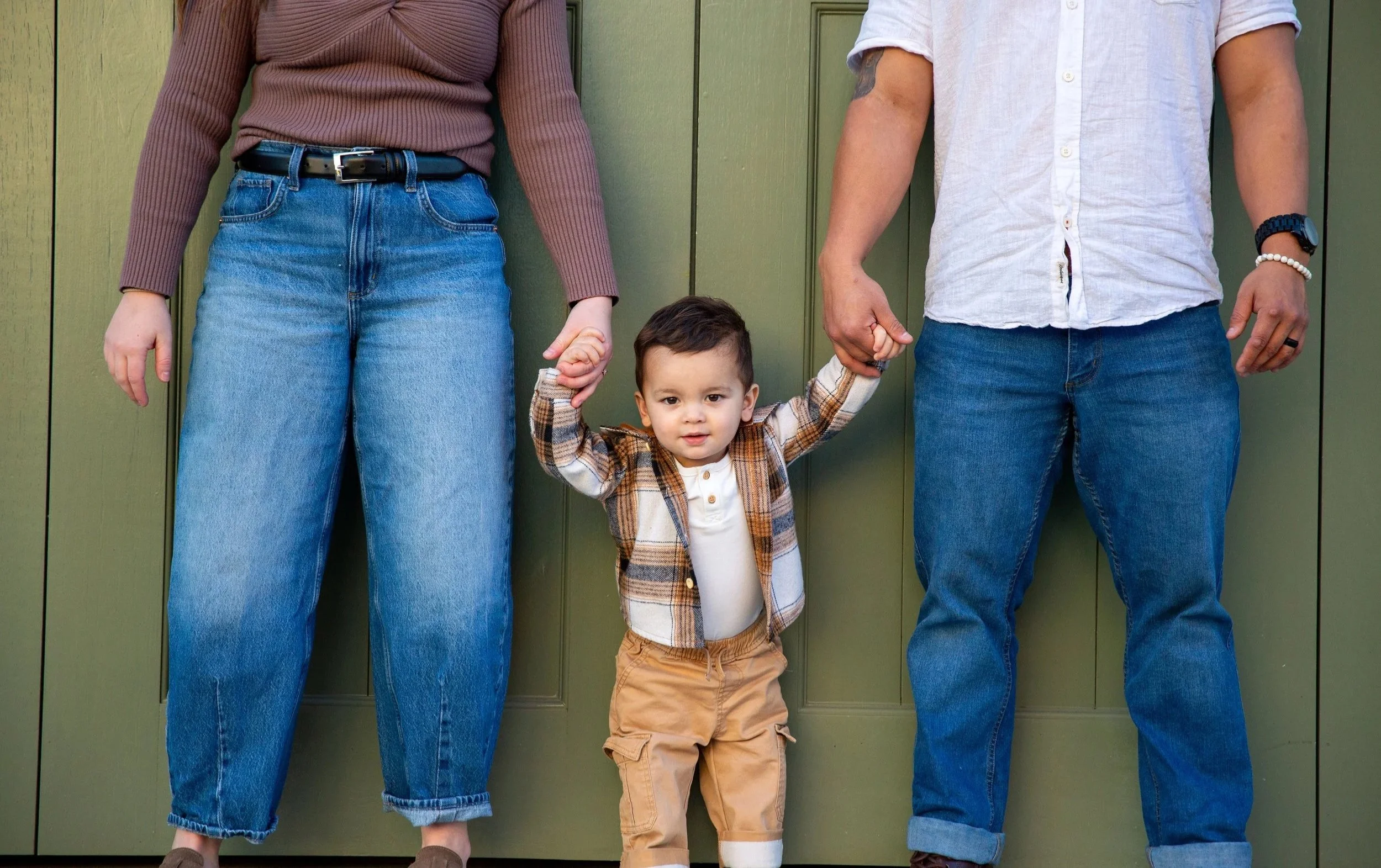 Child holding hands with two adults against a green wall