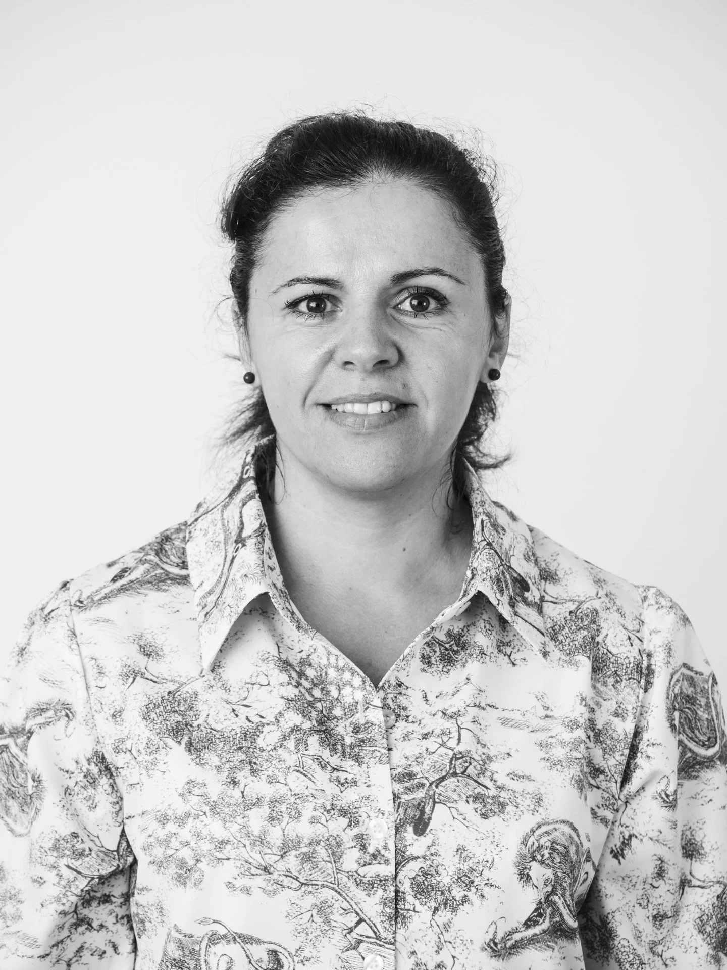 Portrait d'une femme souriante en noir et blanc portant une chemise avec un motif de paysage.