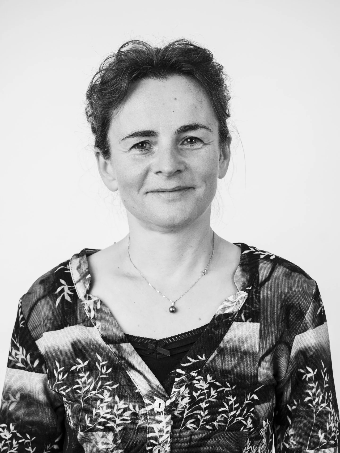 Portrait d'une femme avec des cheveux courts et bouclés, portant un chemisier à motif floral et un collier avec une boule.