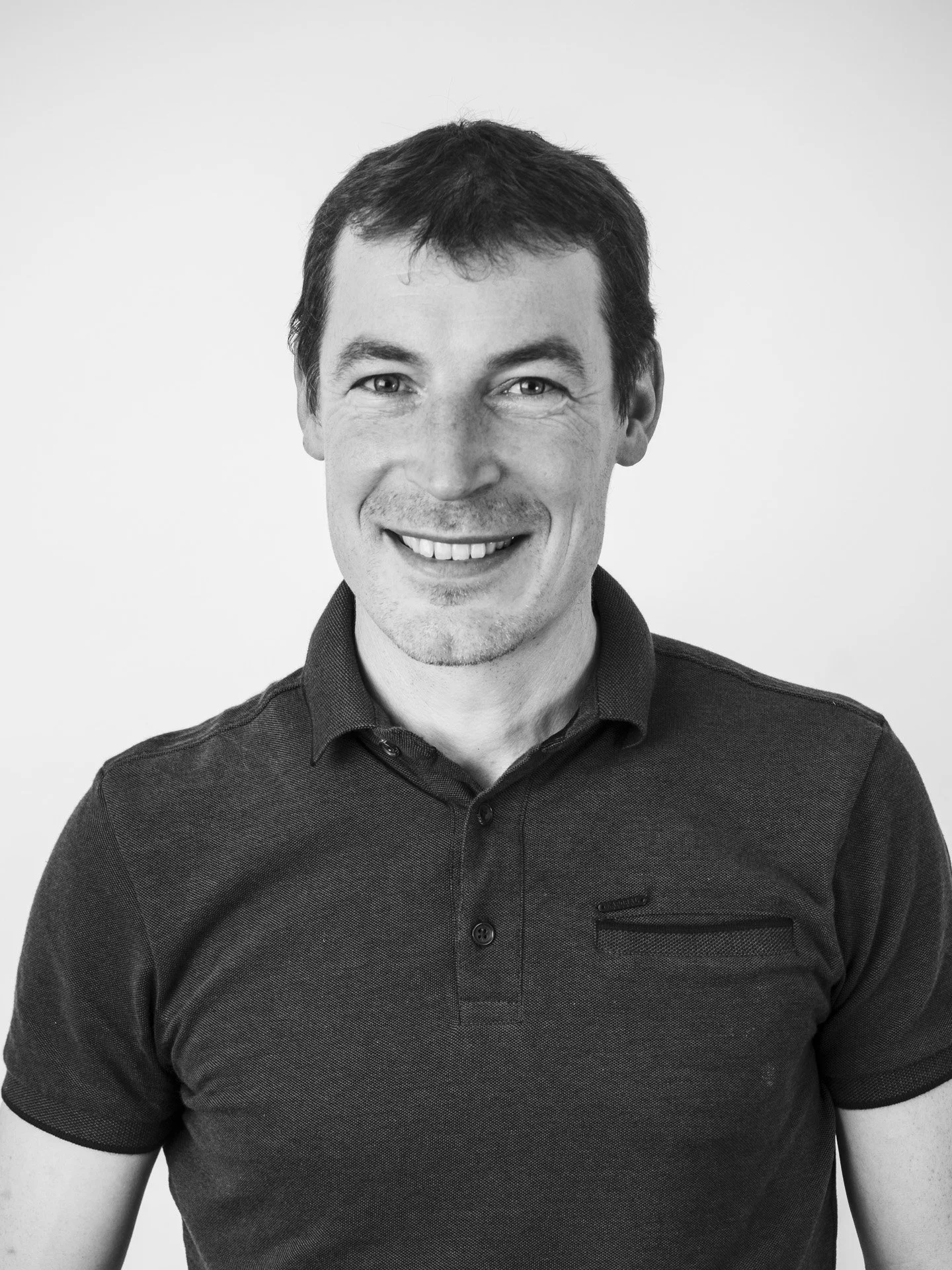 Homme souriant portant un t-shirt noir, portrait en noir et blanc.