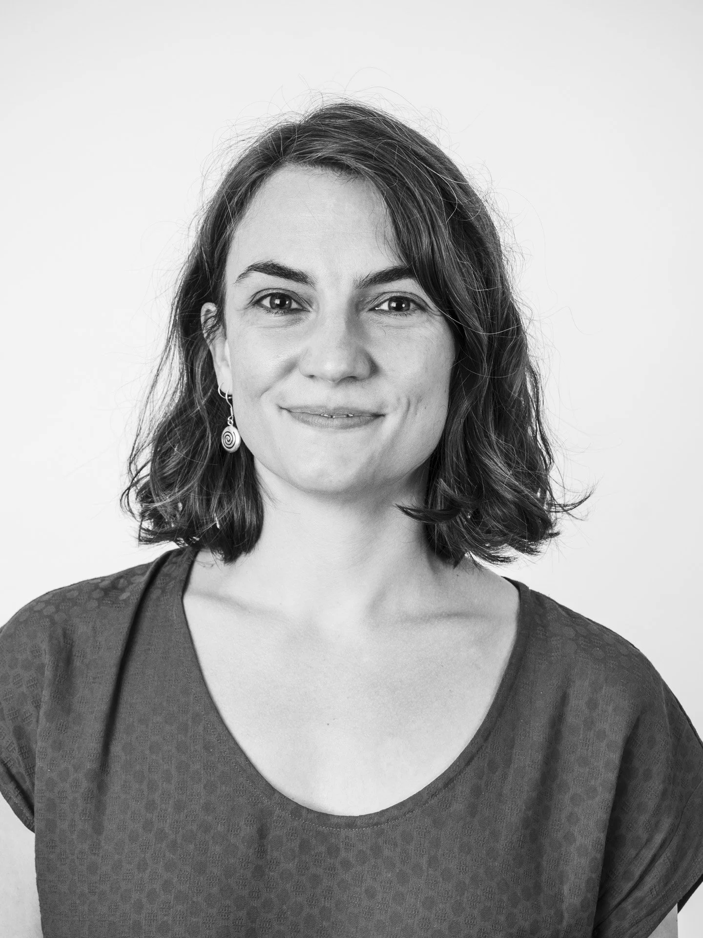 Portrait en noir et blanc d'une femme avec des cheveux bruns ondulés, portant un t-shirt à manches courtes avec un motif léger, portant une boucle d'oreille spiralée.