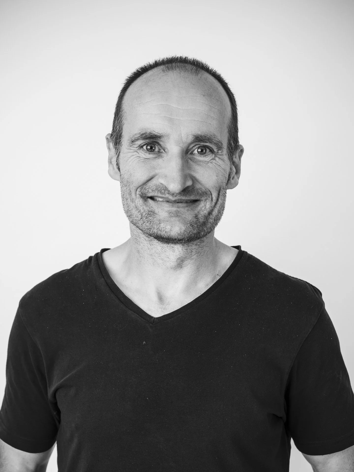 Un homme souriant portant un t-shirt noir, sur fond blanc.