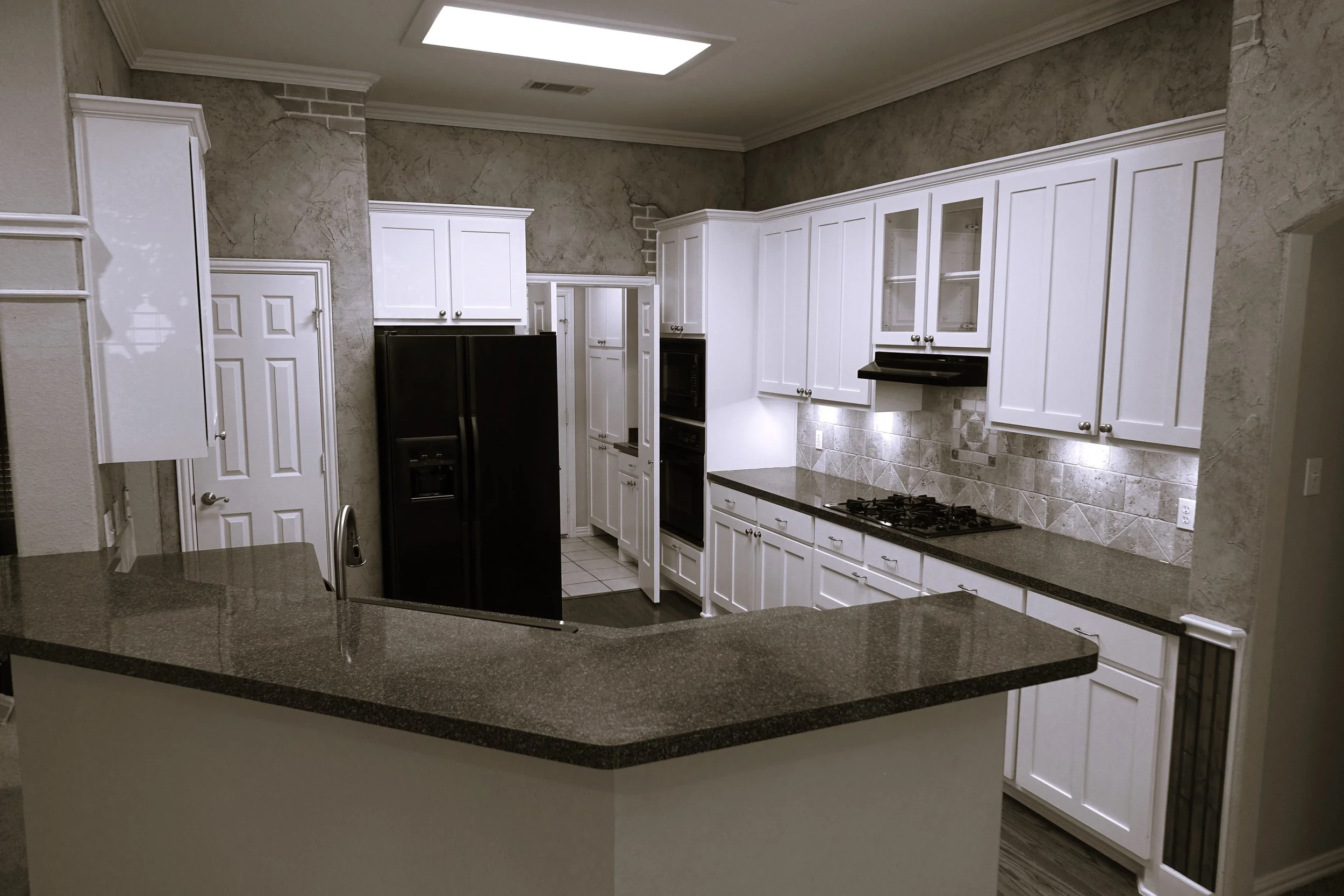 Modern kitchen with white cabinets, black refrigerator, granite countertops, and a tiled backsplash.