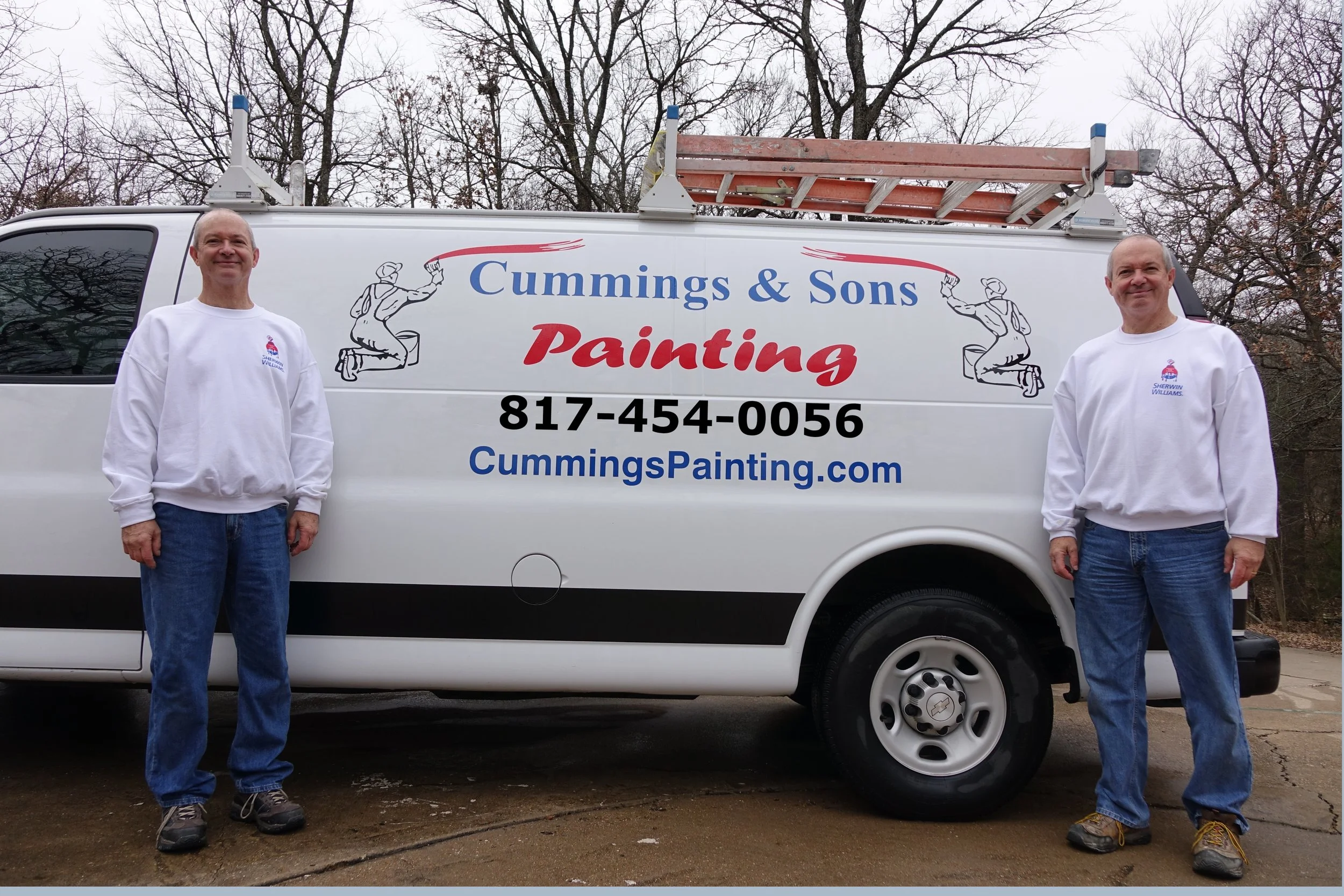 Two men standing in front of a white company van with painting business advertisement on it, wearing white sweatshirts and jeans, with a ladder on top of the van. The van displays text: 'Cummings & Sons Painting', a phone number, and a website.