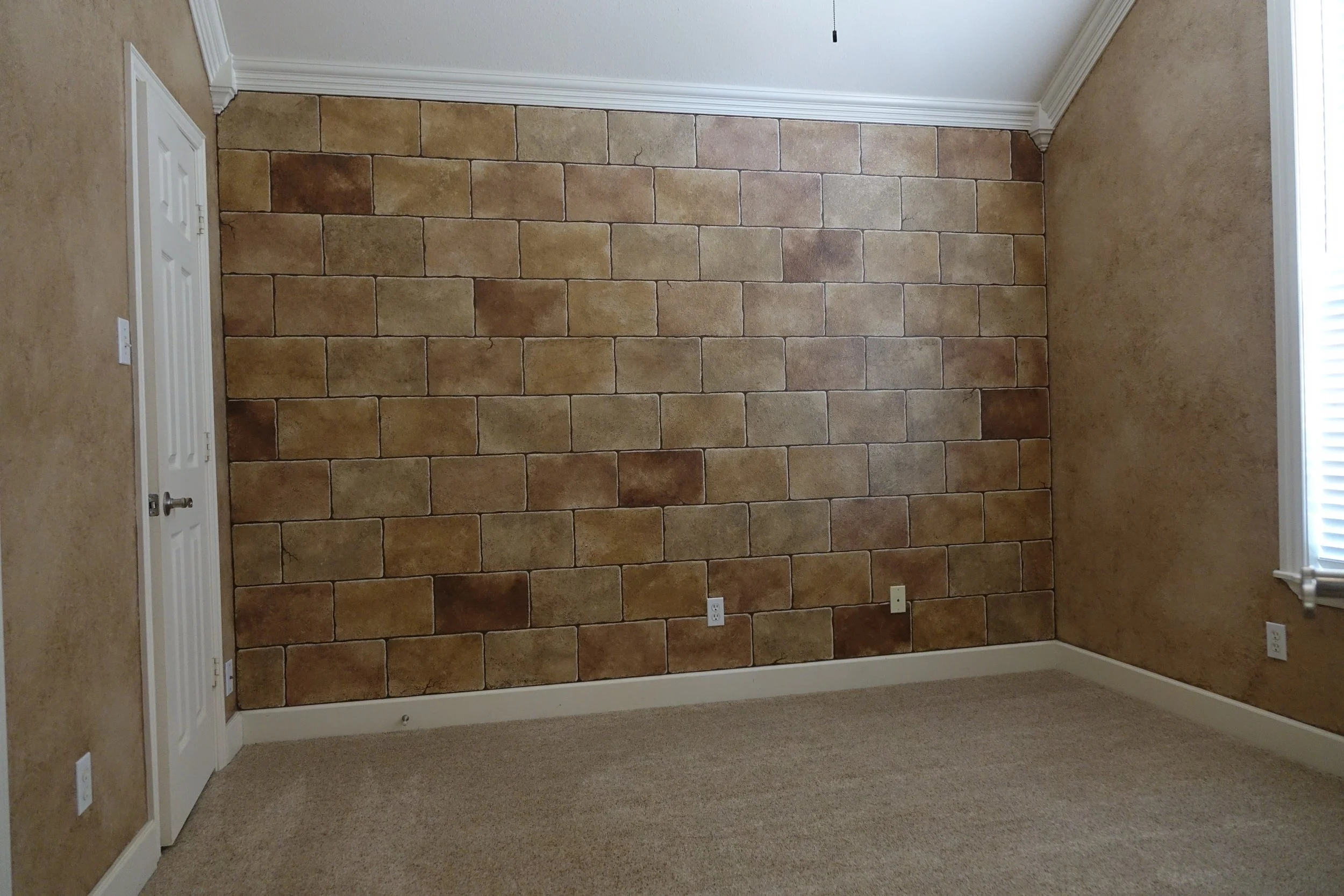 Empty beige carpeted room with a stone accent wall, a white door, and a window with blinds.