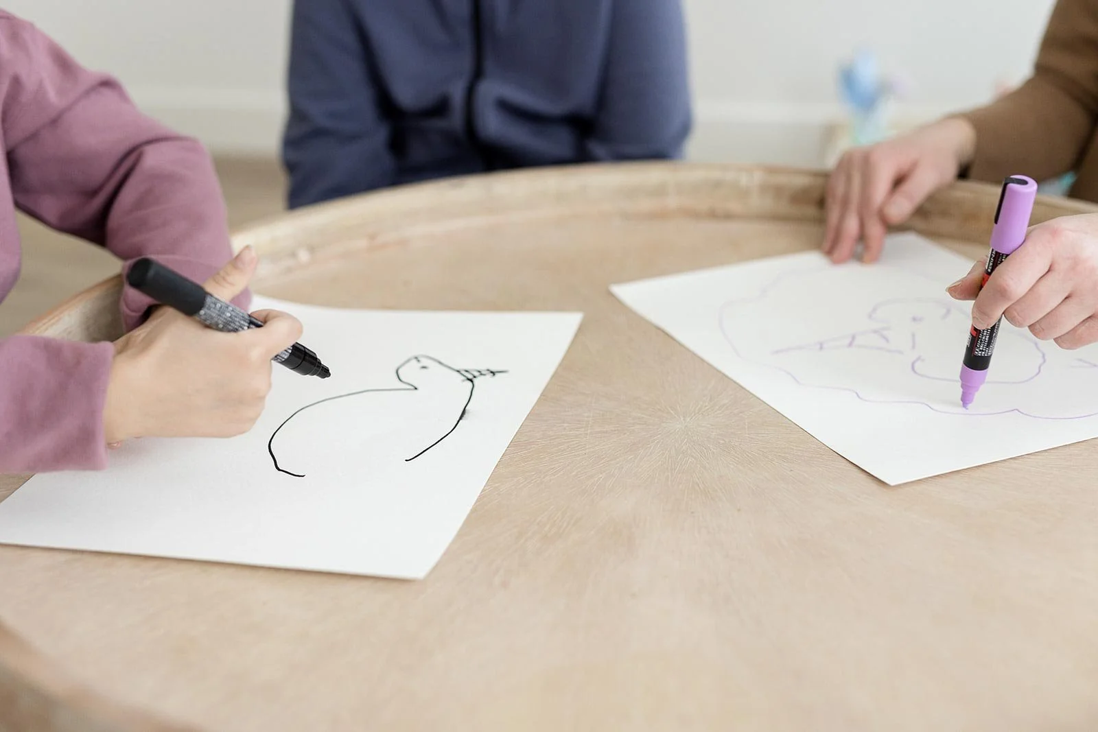 Two children drawing side by side with markers at a table during a sibling session at Creative Sky Psychology in Calgary.
