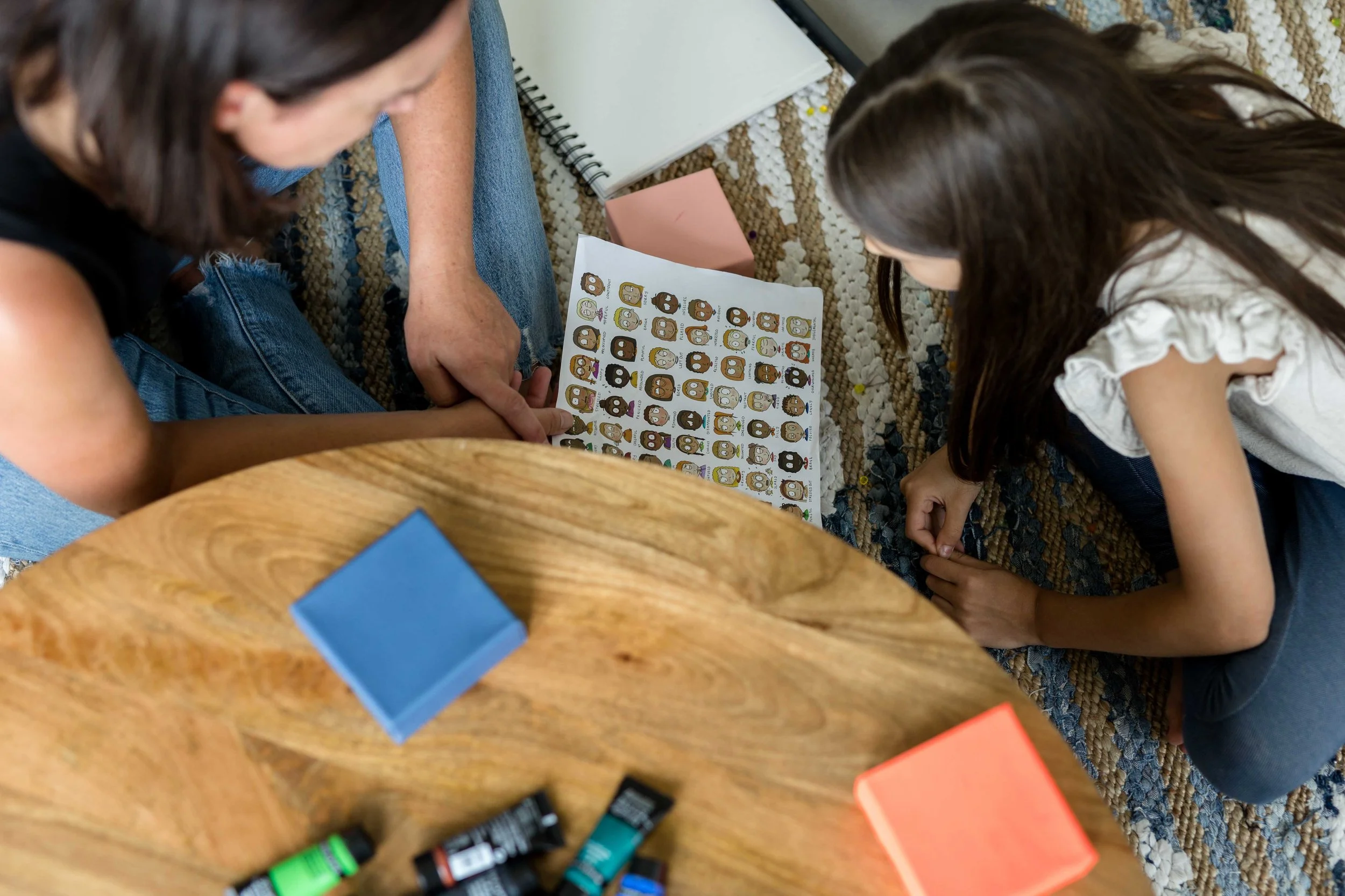 A child psychologist and child sitting together at a table with an emotions chart and notebooks during a session at Creative Sky Psychology in Calgary.