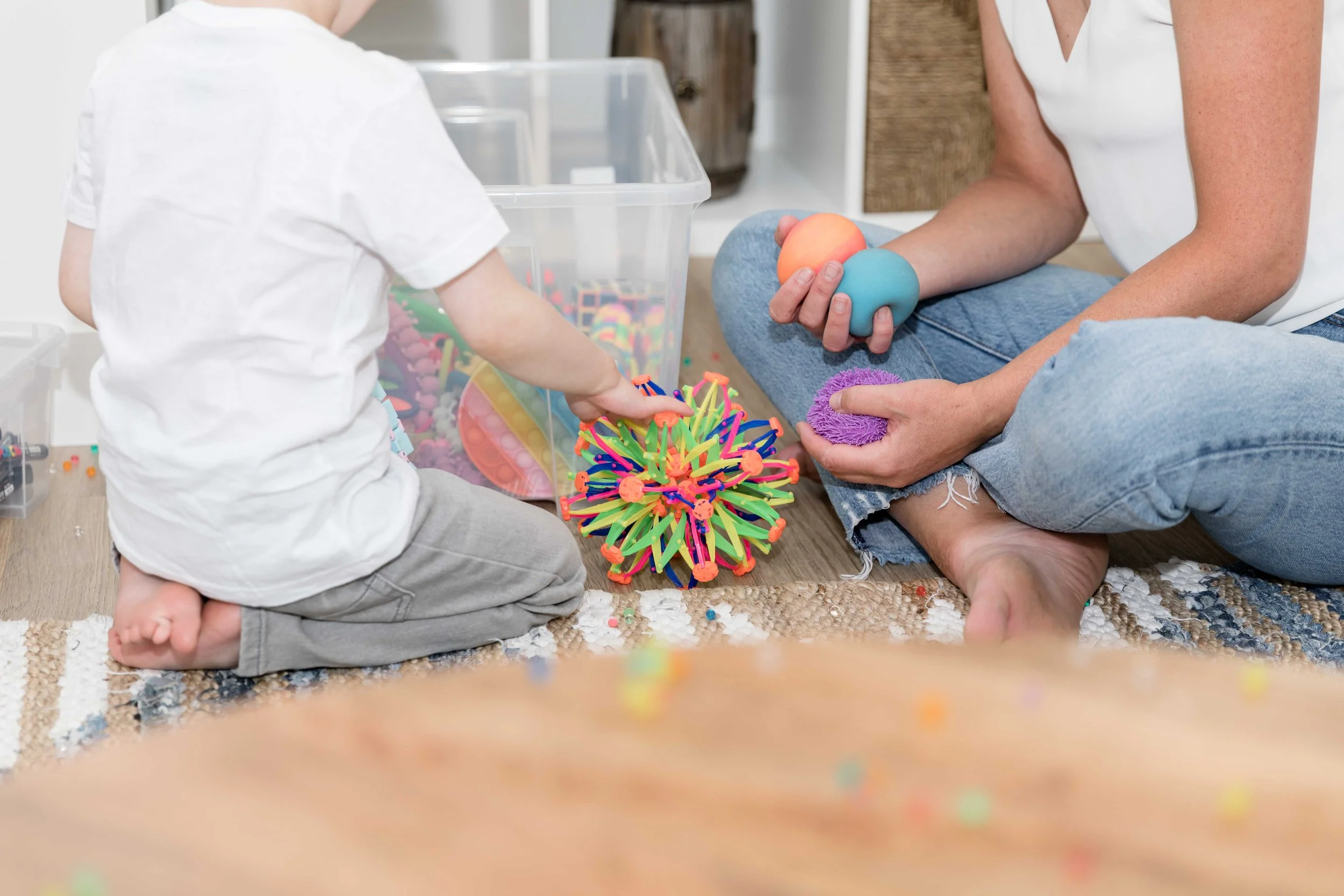 A child psychologist and child sitting on the floor playing with colourful sensory toys during a therapy session at Creative Sky Psychology in Calgary