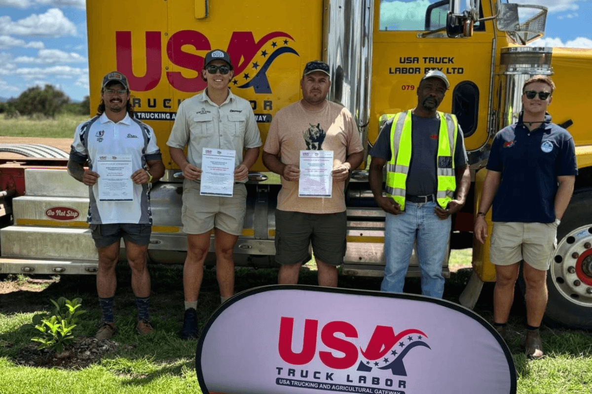 candidates for H-2A jobs after completing USA Truck Labor's training program, standing in front of yellow peterbilt training truck