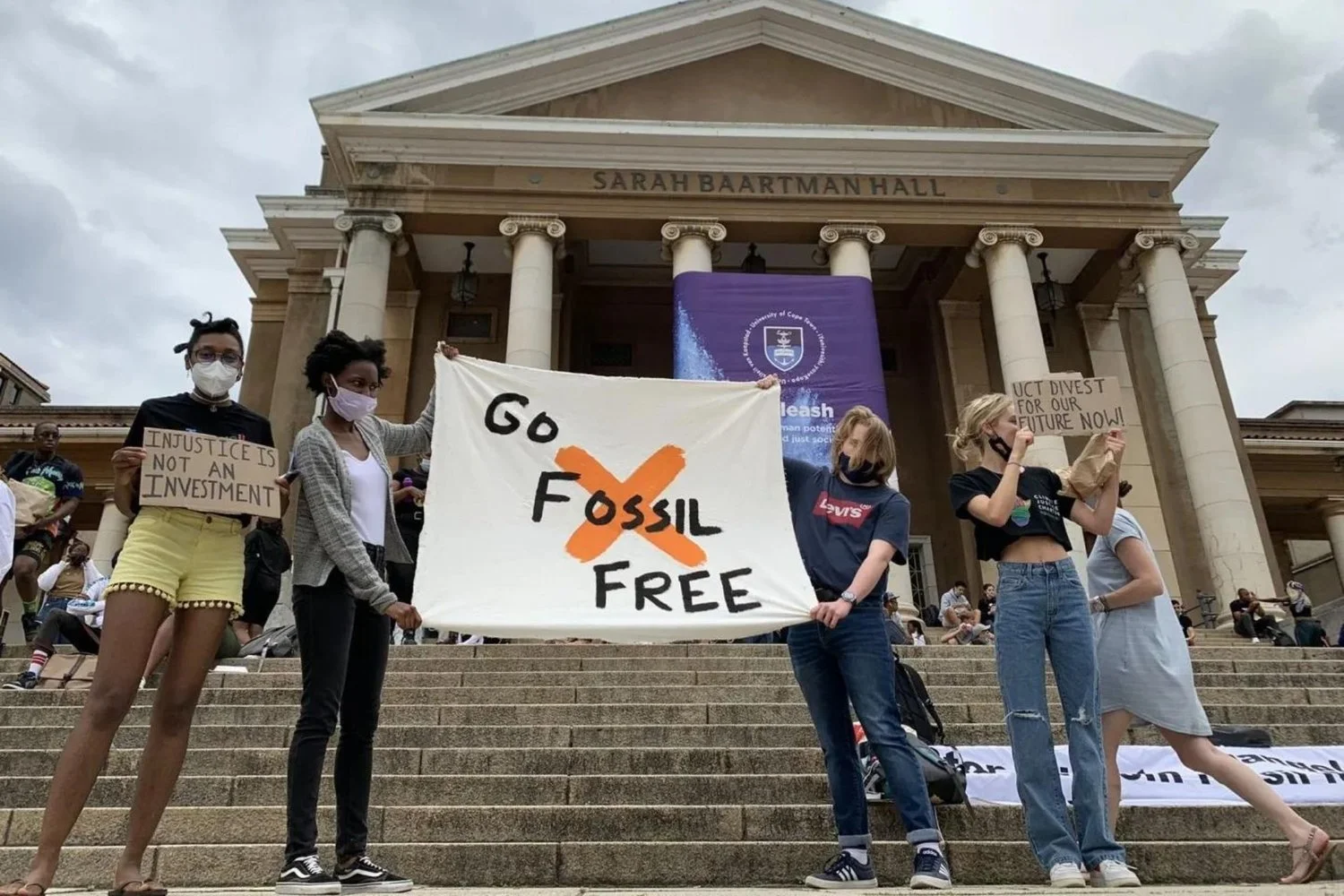 Students holding protest signs, including "Go Fossil Free" and "Injustice is Not an Investment," in front of Sarah Baartman Hall.
