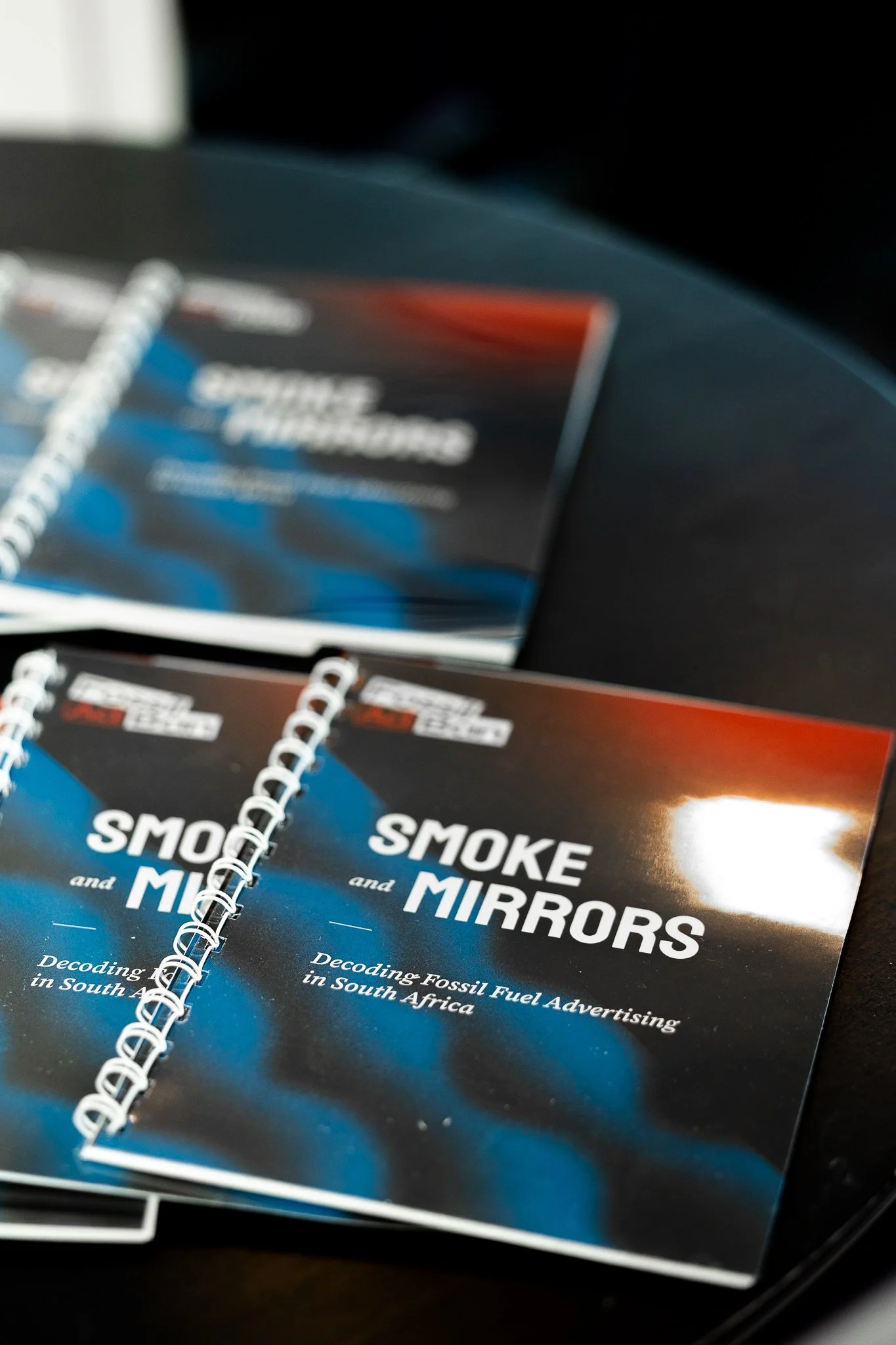 Booklets titled 'Smoke and Mirrors: Decoding Fossil Fuel Advertising in South Africa' on a table
