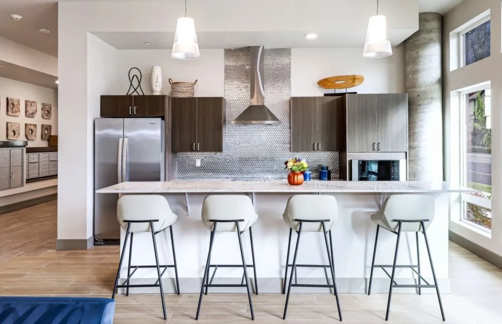 Interior view of kitchen featuring a bar-height counter, seating, wood cabinets, stainless appliances, and large windows.