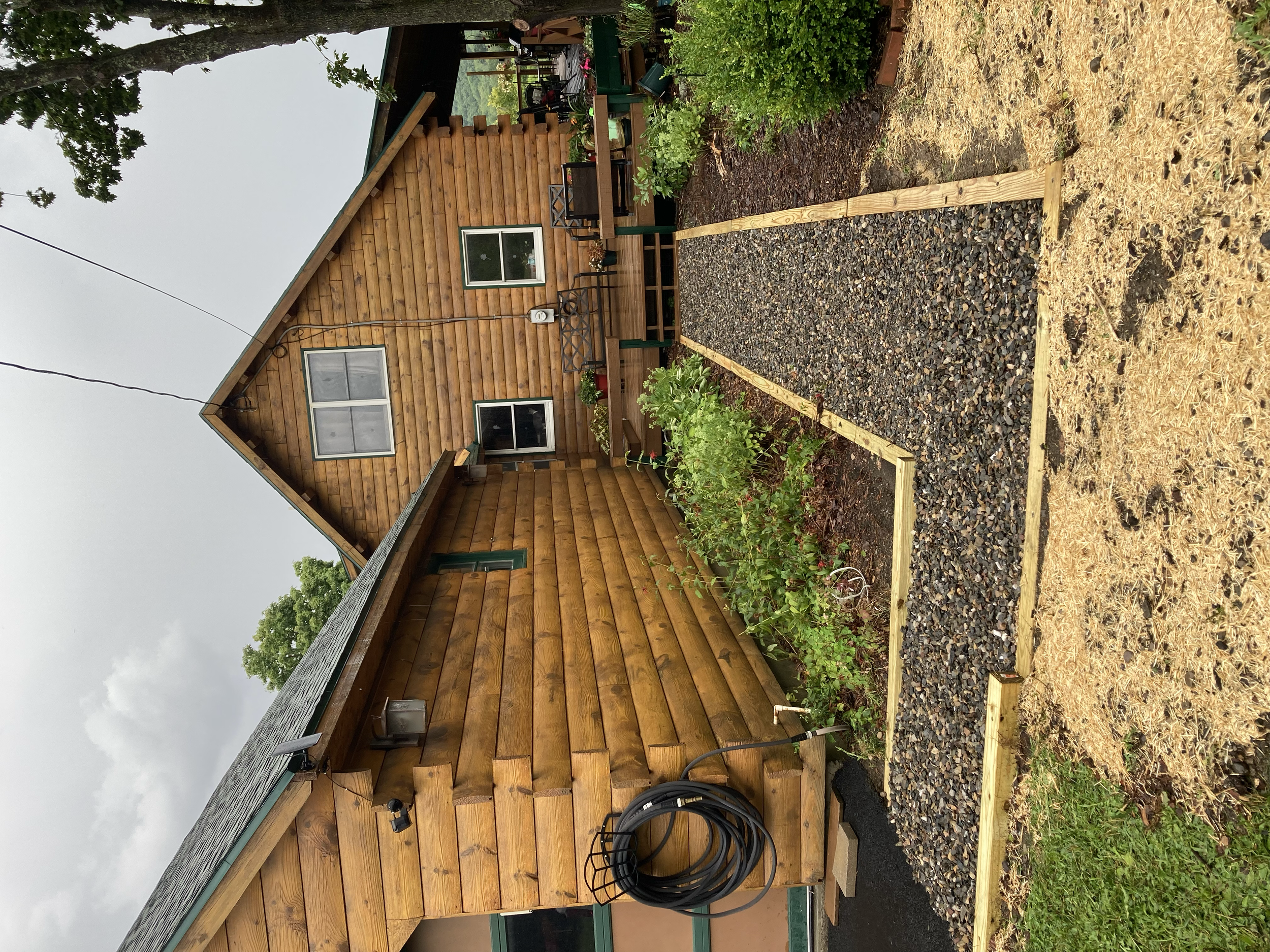 A wooden house with a garden bed and gravel path in the backyard during a cloudy day.