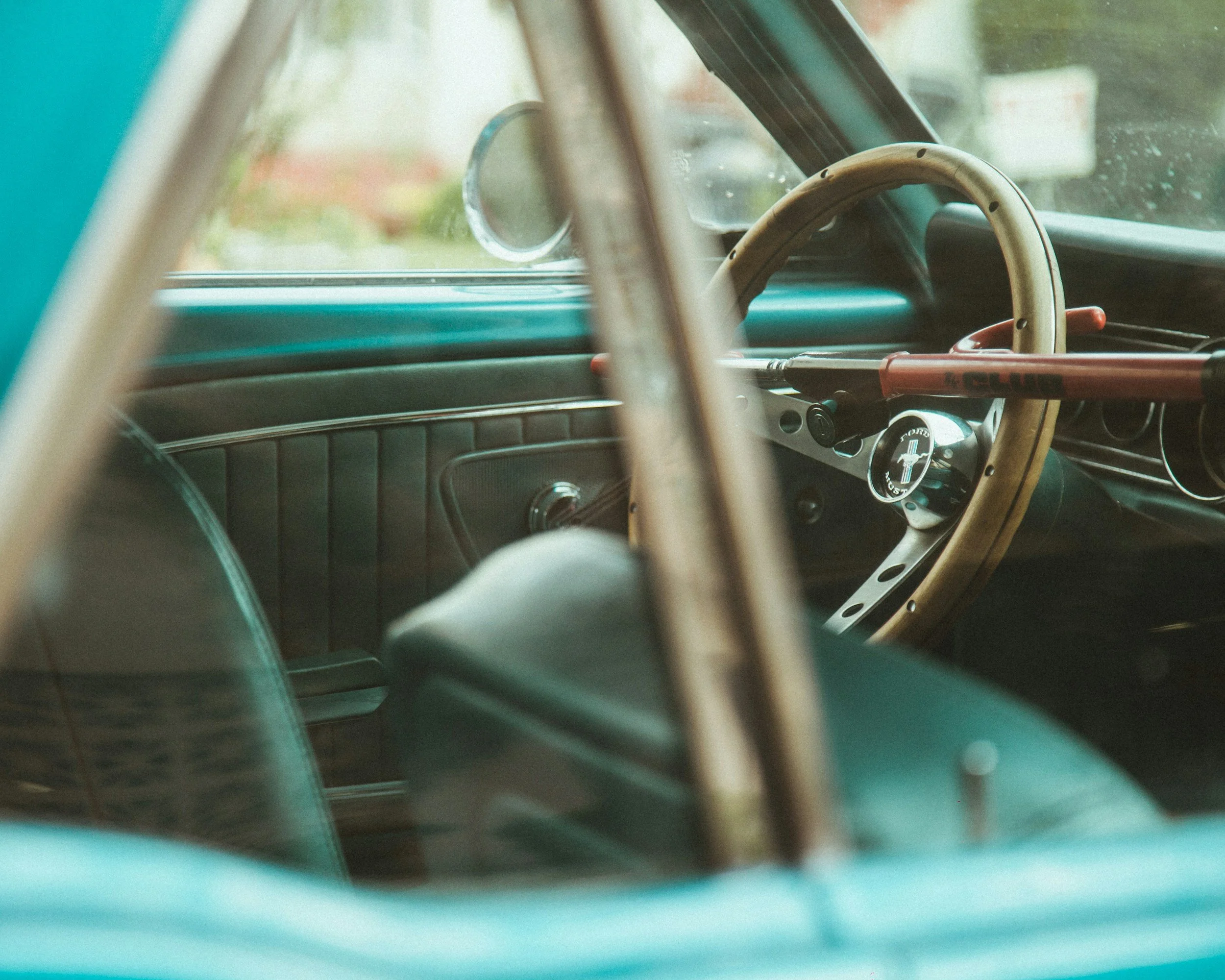 Interior view of a vintage car showing a wooden steering wheel with a locking device, door panel, and side mirror.