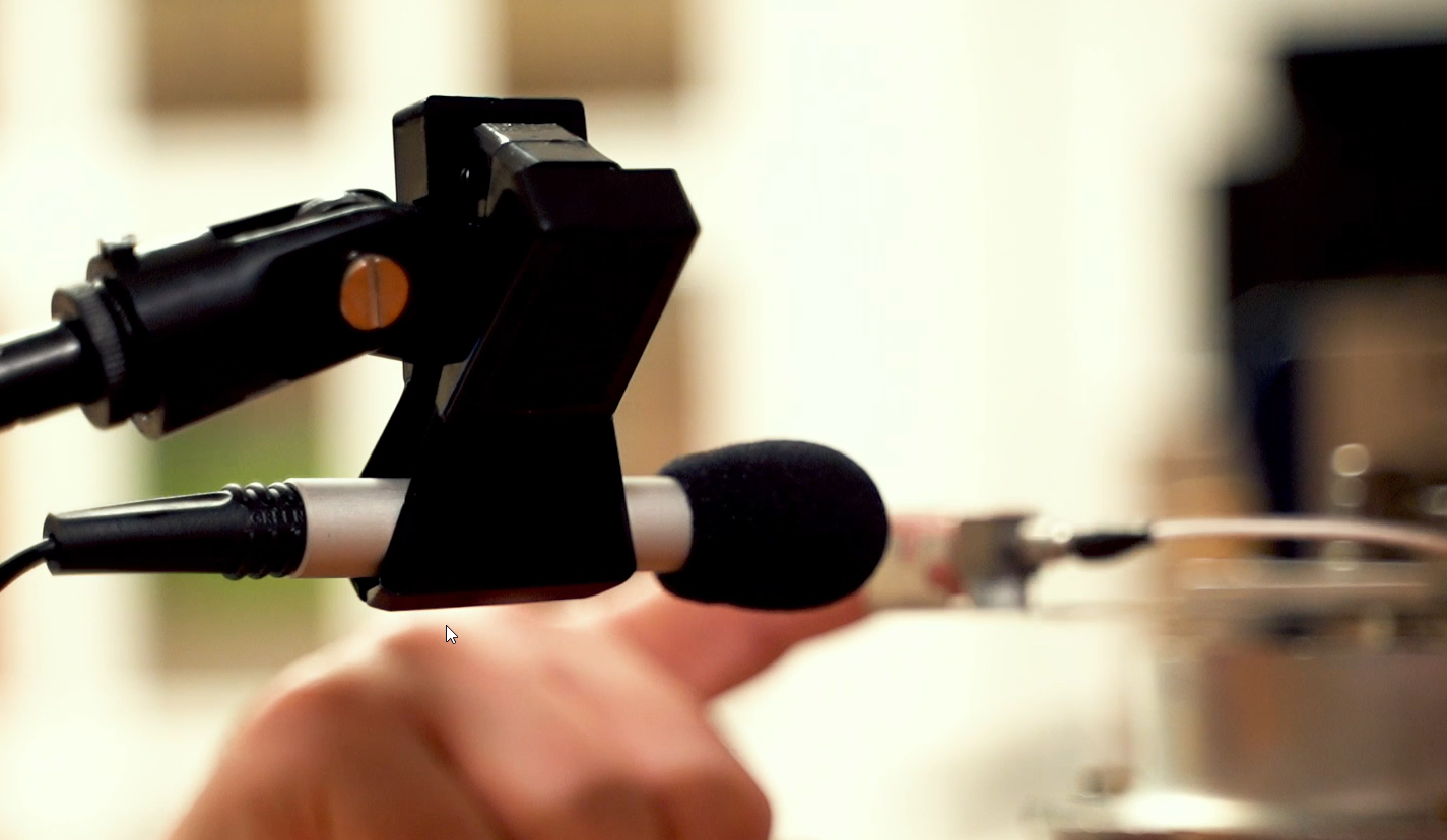 Microfono collegato a un registratore audio o videocamera, con sfondo sfocato.