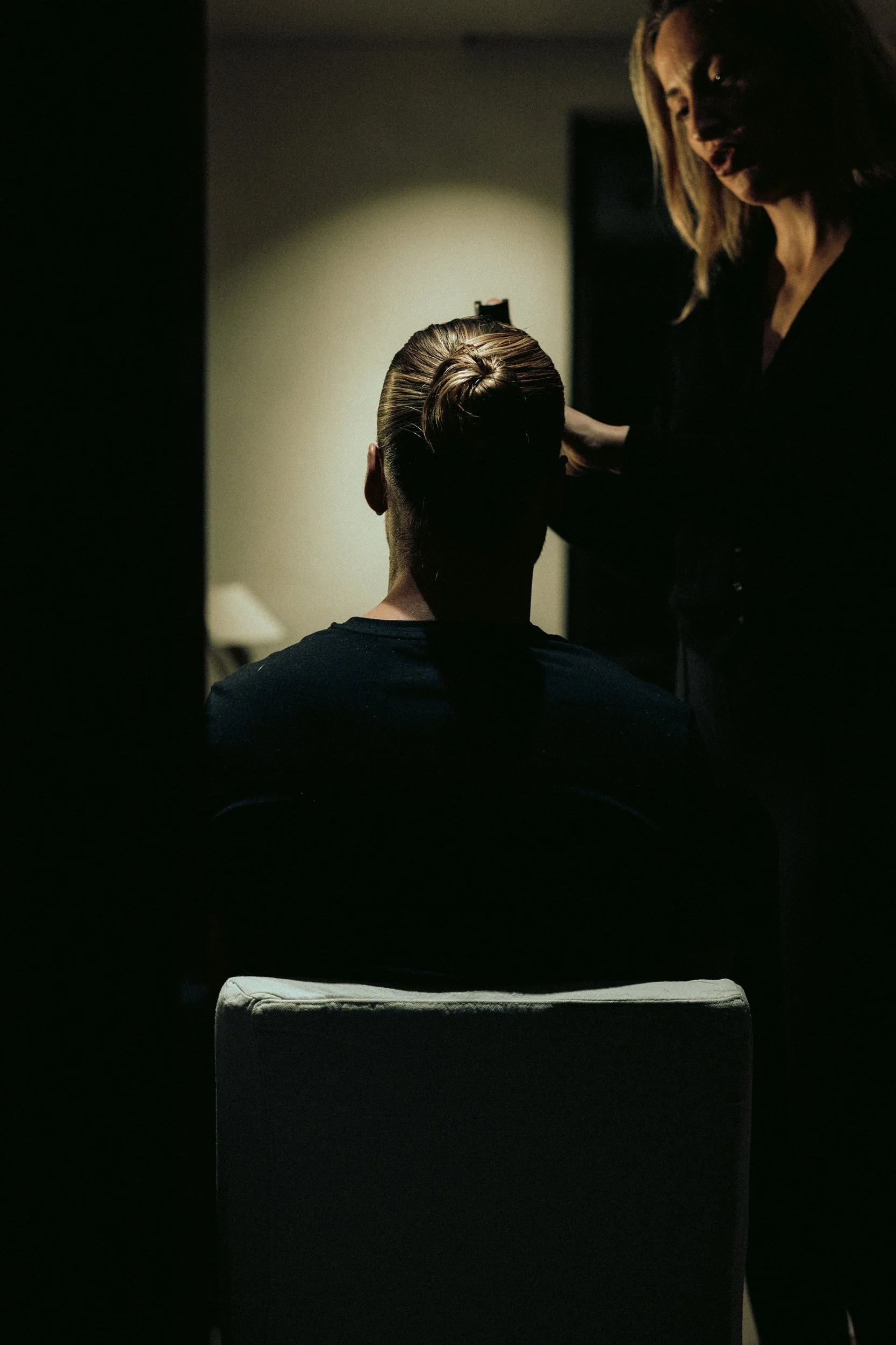 Ein Mann (Rurik Gislason) lässt sich im Dunkeln die Haare stylen, während eine Stylistin neben ihr steht.