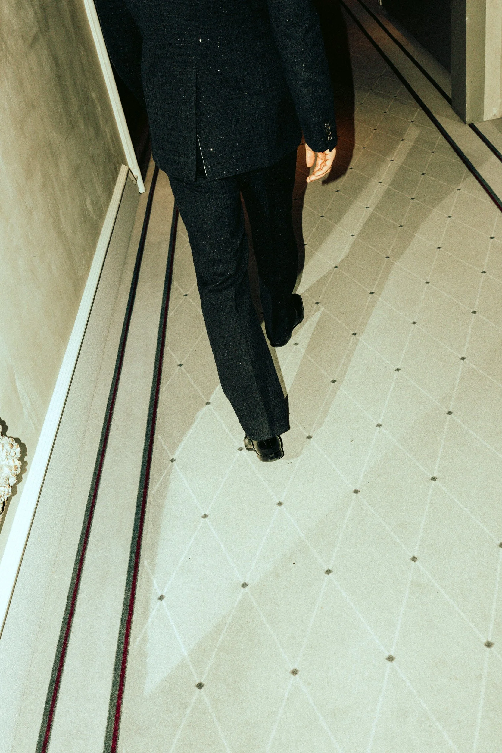 Nahaufnahme eines Mannes (Rurik Gislason) in einem schwarzen Anzug, der durch einen Flur geht.