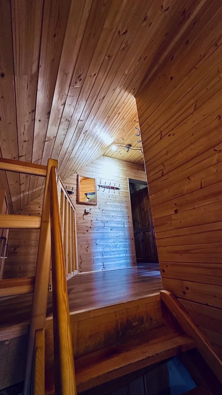 Wood-paneled interior with stairs, a mirror, hooks, and a doorway.