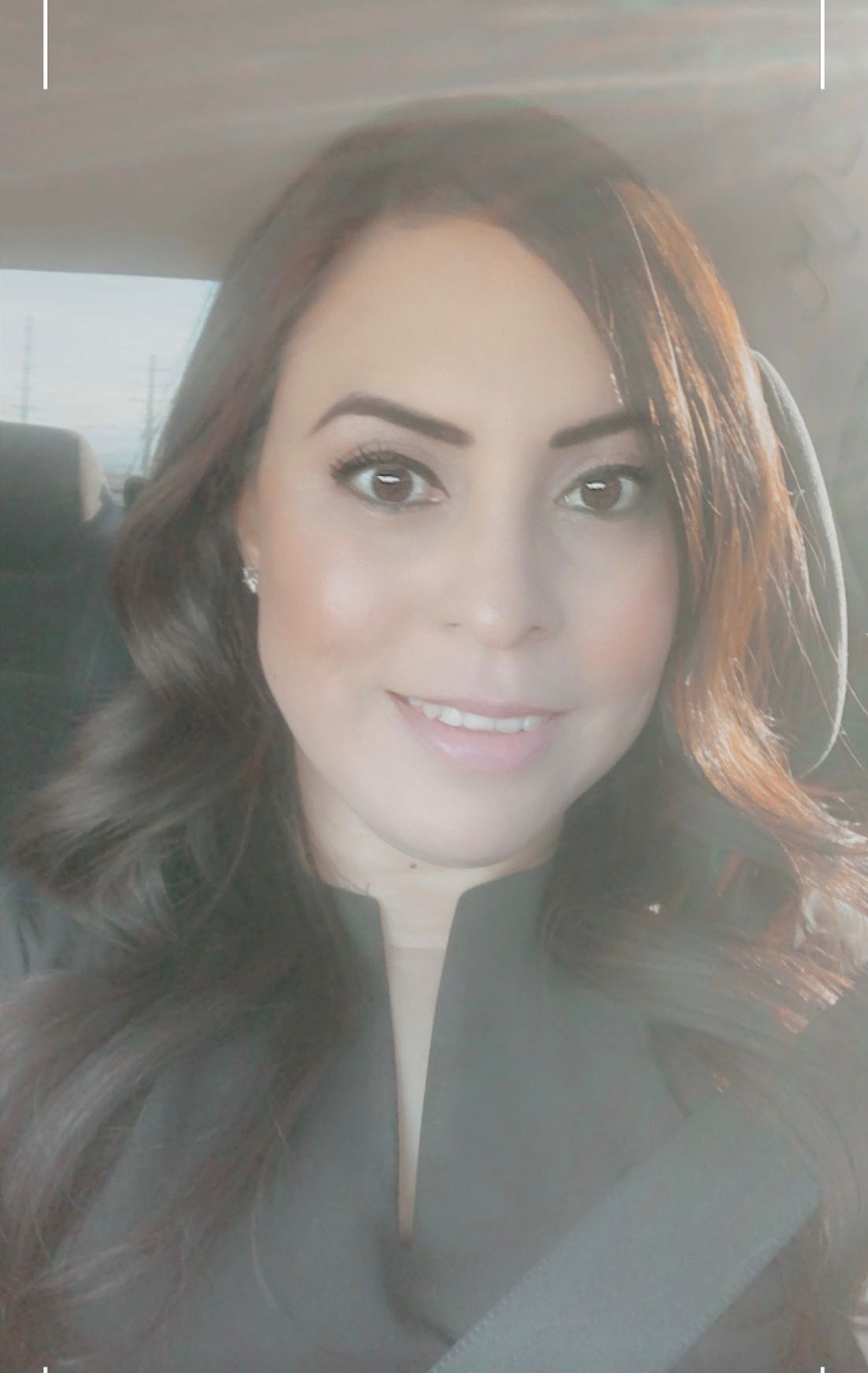 A woman with long, wavy brown hair taking a selfie inside a car.