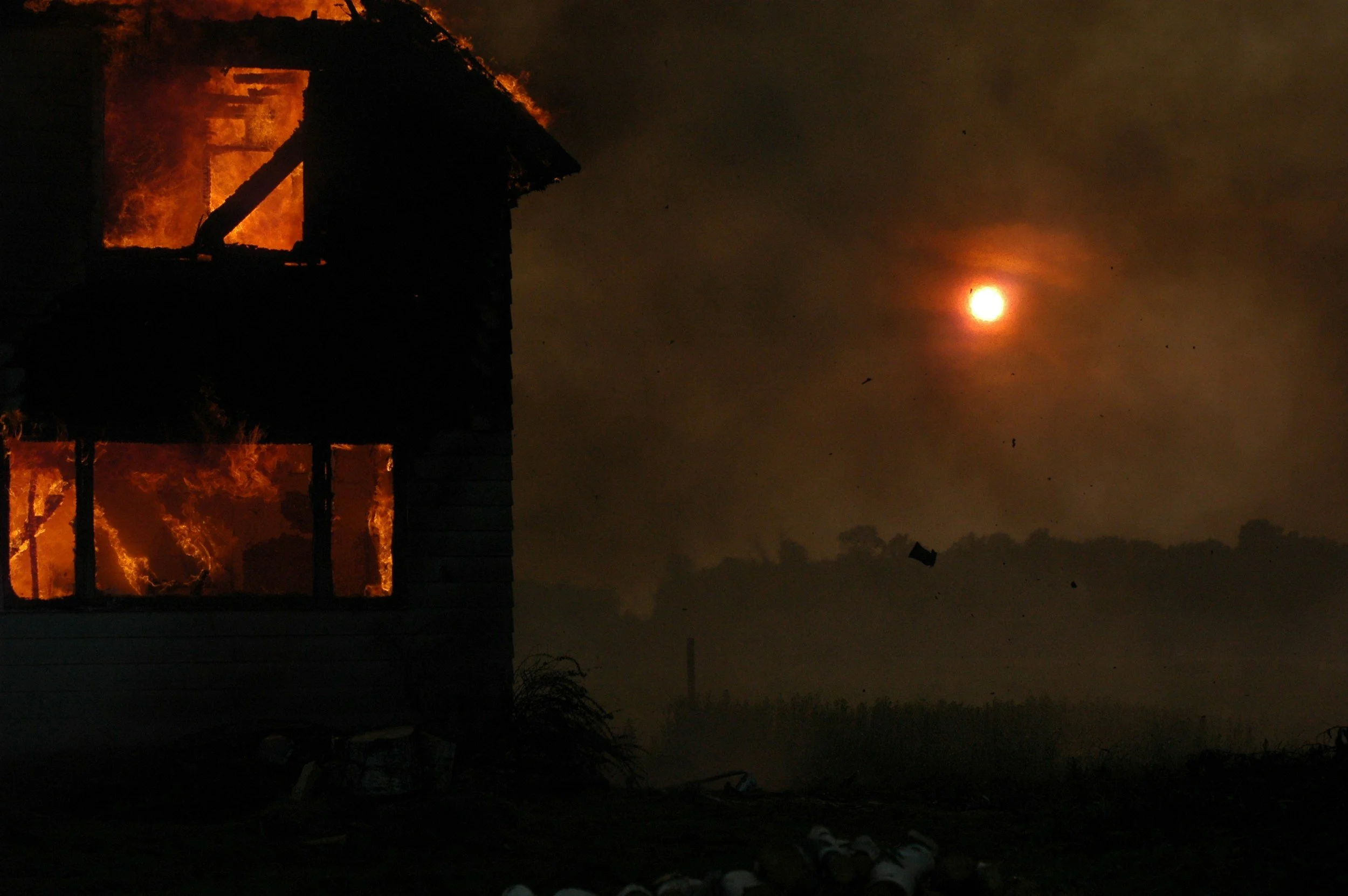 Image of a burning home with the sun shining through hazy smoke in the background