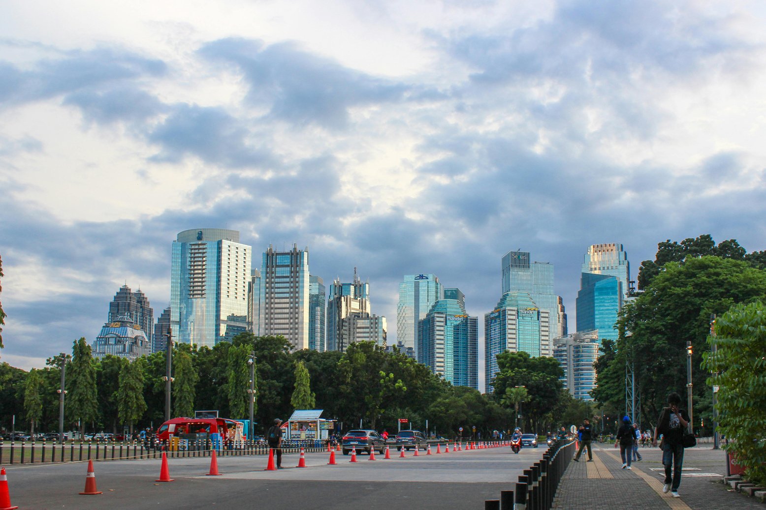 Daytime view of several skyscrapers in Jakarta, Indonesia with cars and people in the foreground
