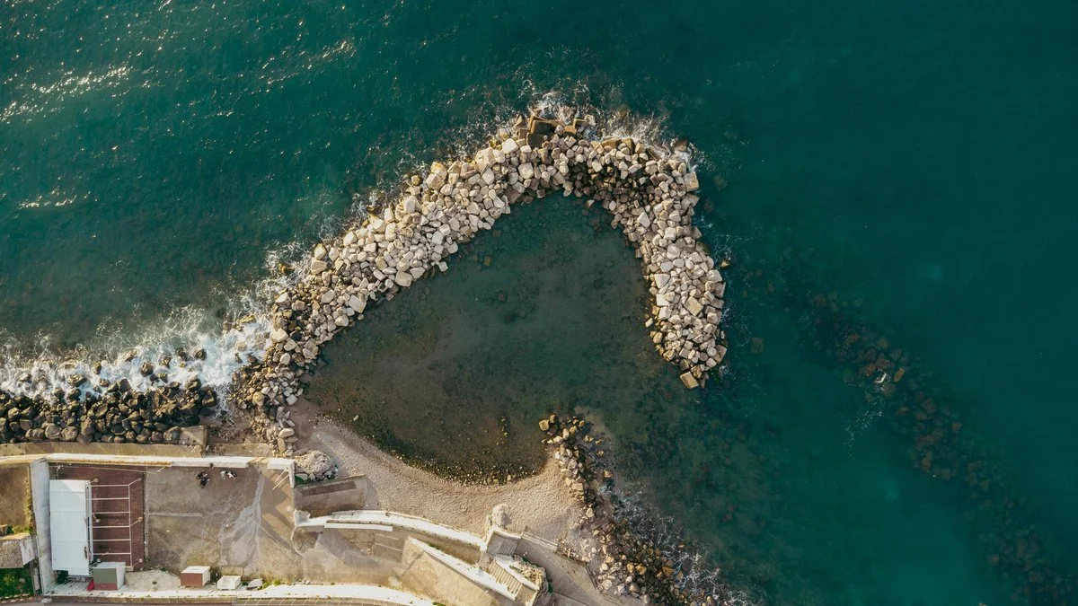 Image of a headland breakwater constructed of stone and disrupting waves close to shore
