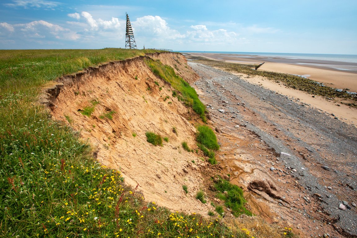 View of shoreline with nearby meadow displaying signs of erosion