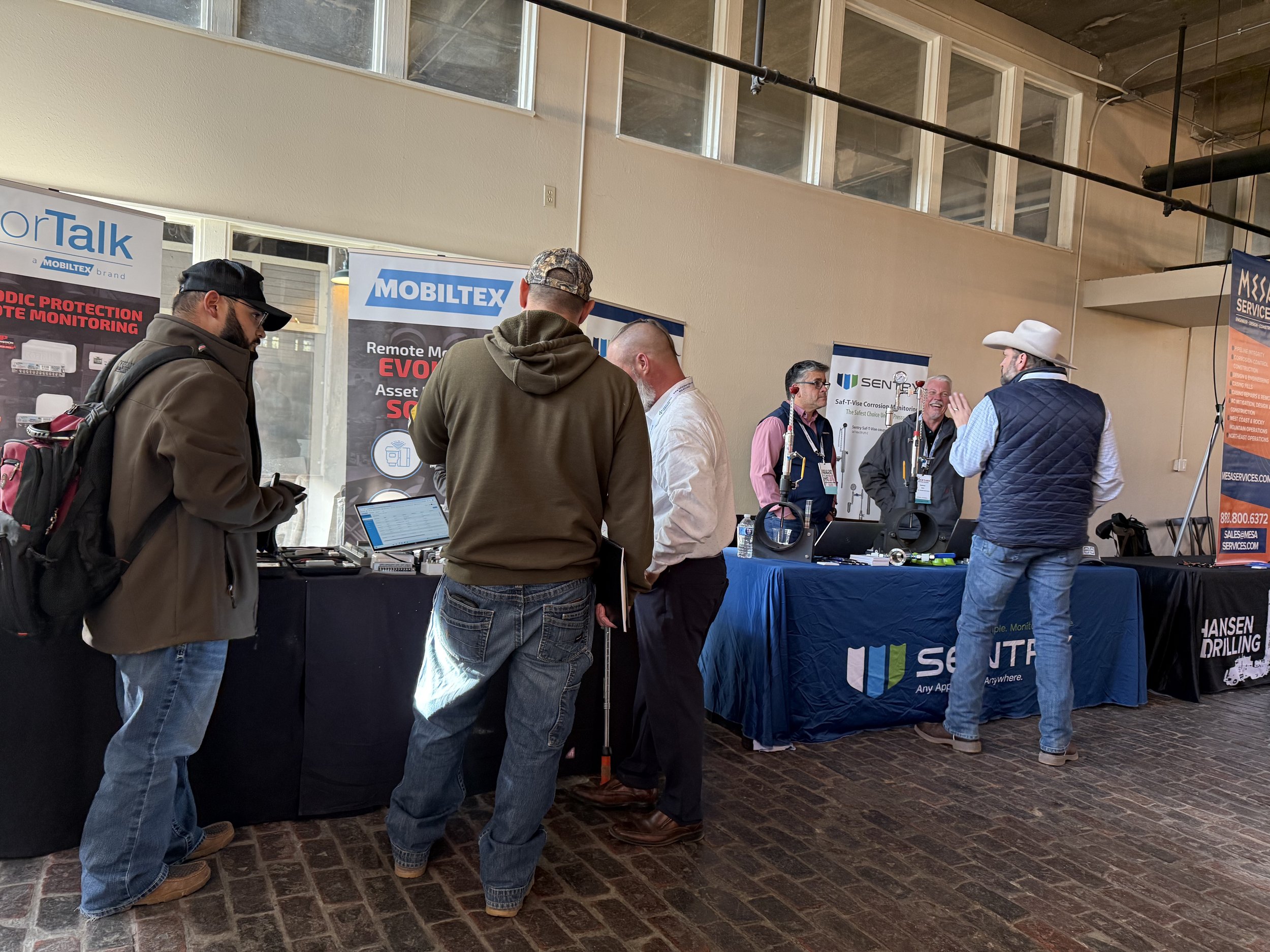 People at a trade show booth discussing various tech products, with banners and tables displaying company information.
